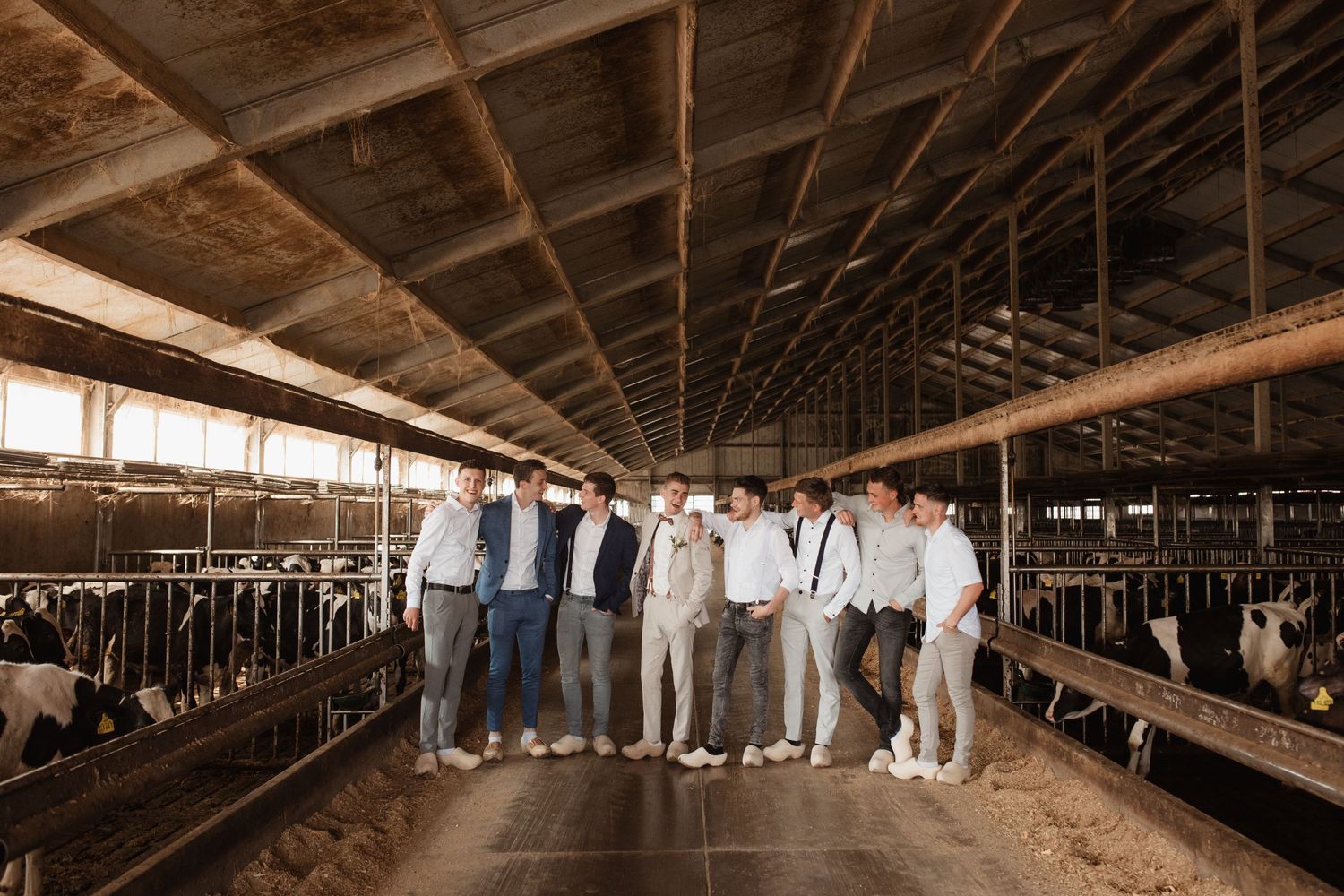 Wedding party members stand in a rustic wooden barn interior with natural lighting.