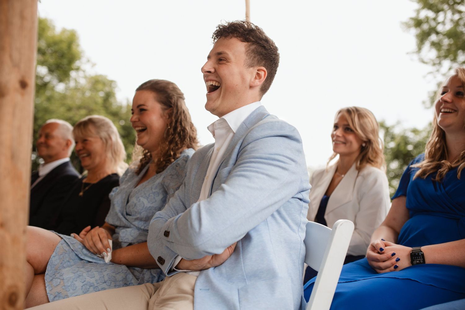 Wedding guests seated in rows watch ceremony with smiles and emotional reactions.