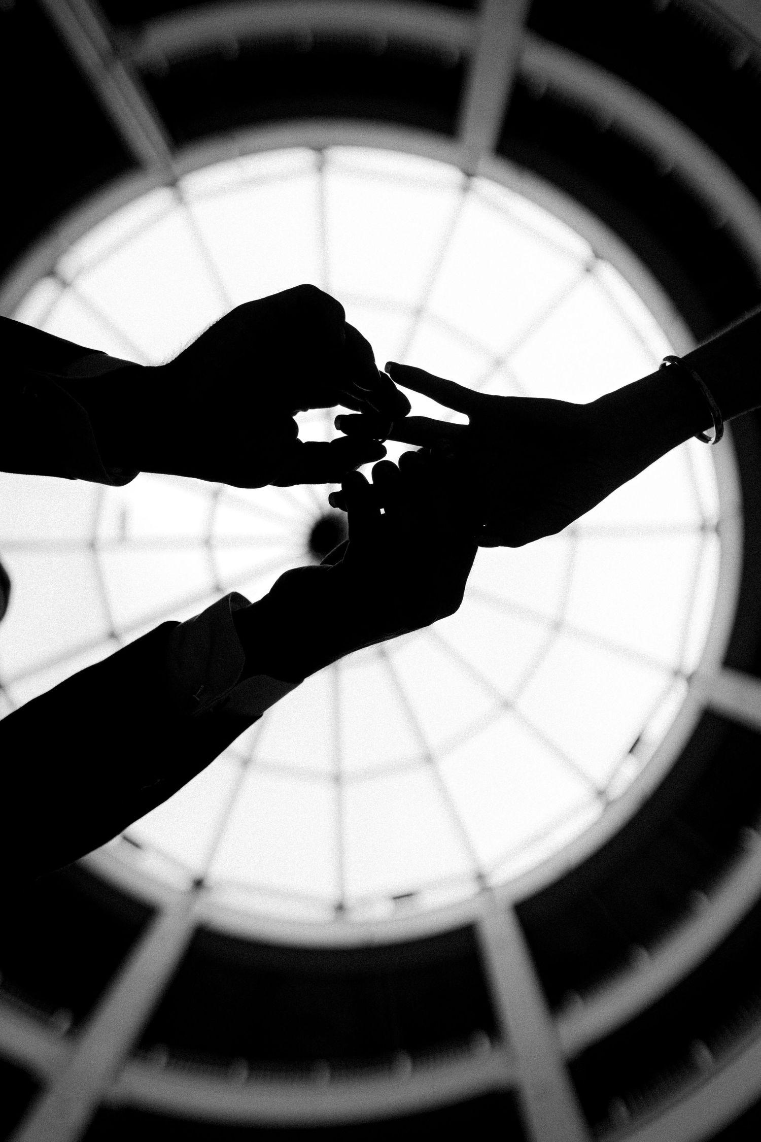 A silhouetted exchange of rings beneath a circular skylight.