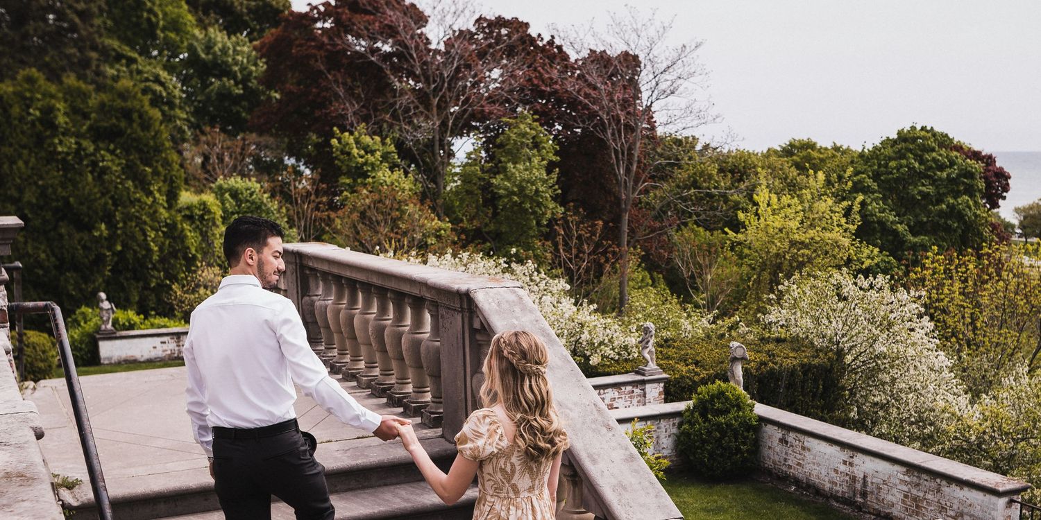 A couple walking along a stone balustrade surrounded by spring foliage.
