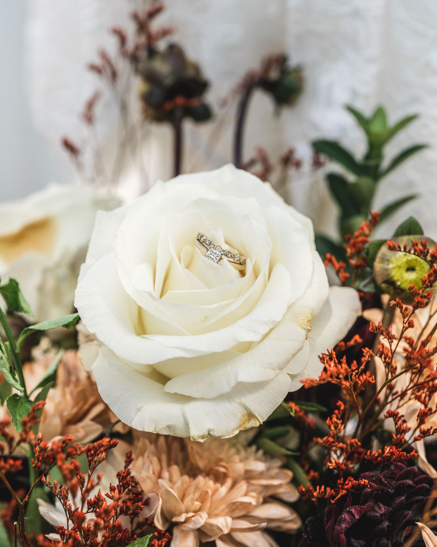 Close-up of a white rose with rustic dried flowers in a romantic wedding arrangement.
