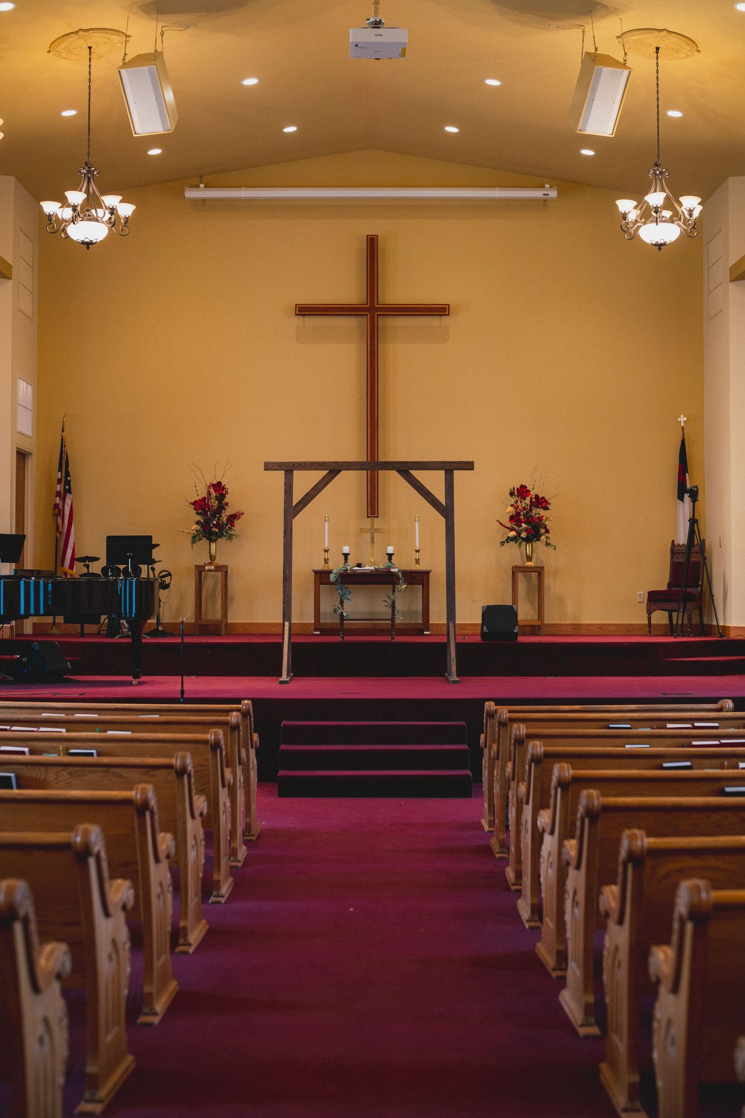 Interior of a church sanctuary with wooden pews and cross centered on yellow wall.