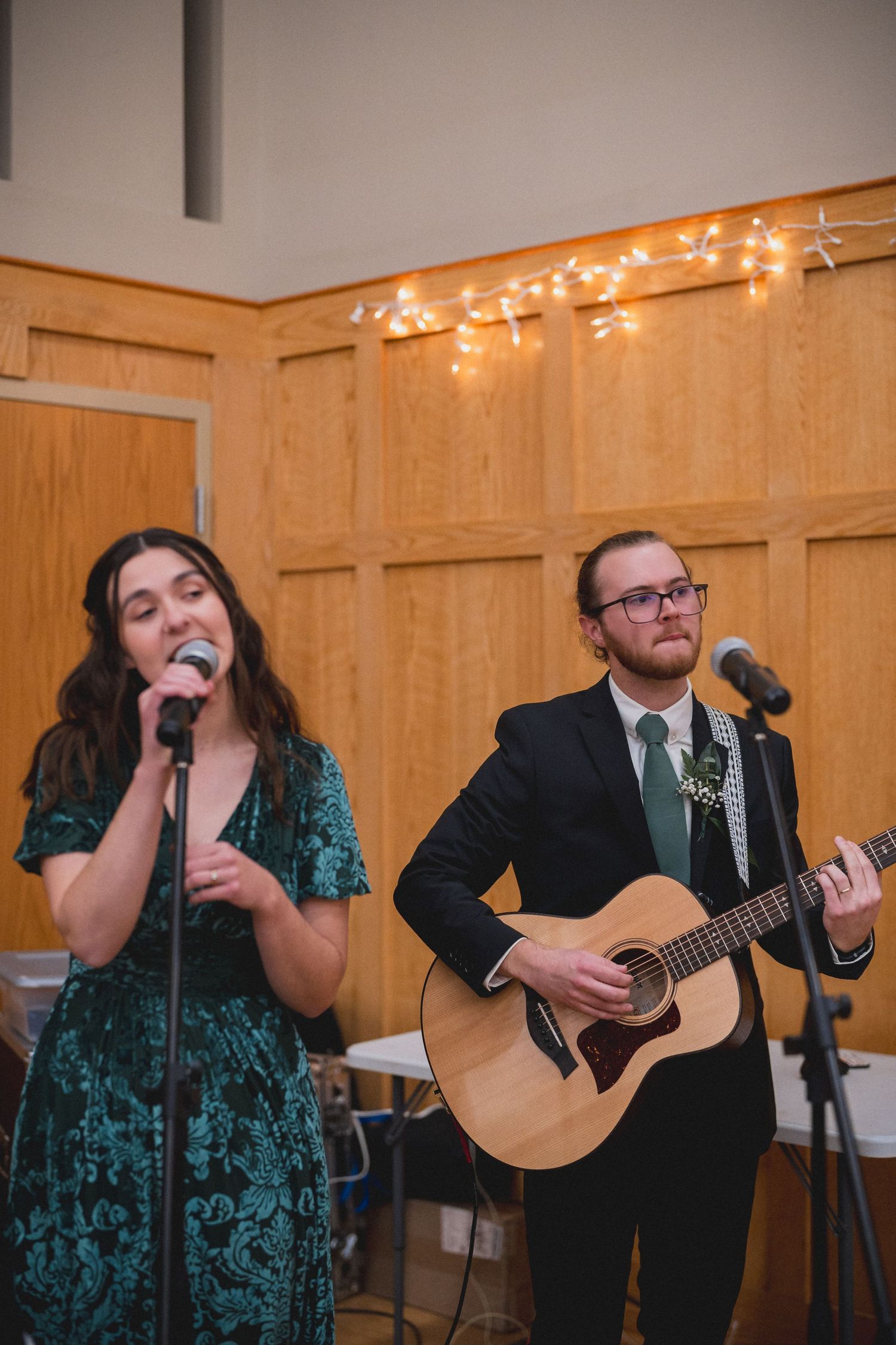 Musicians perform at a wedding reception with a singer in green dress and guitarist in black suit.