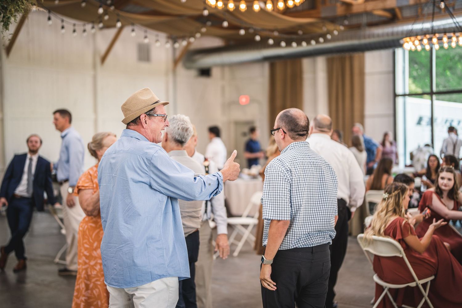 Wedding guests dancing together in an elegant indoor reception venue with string lights.