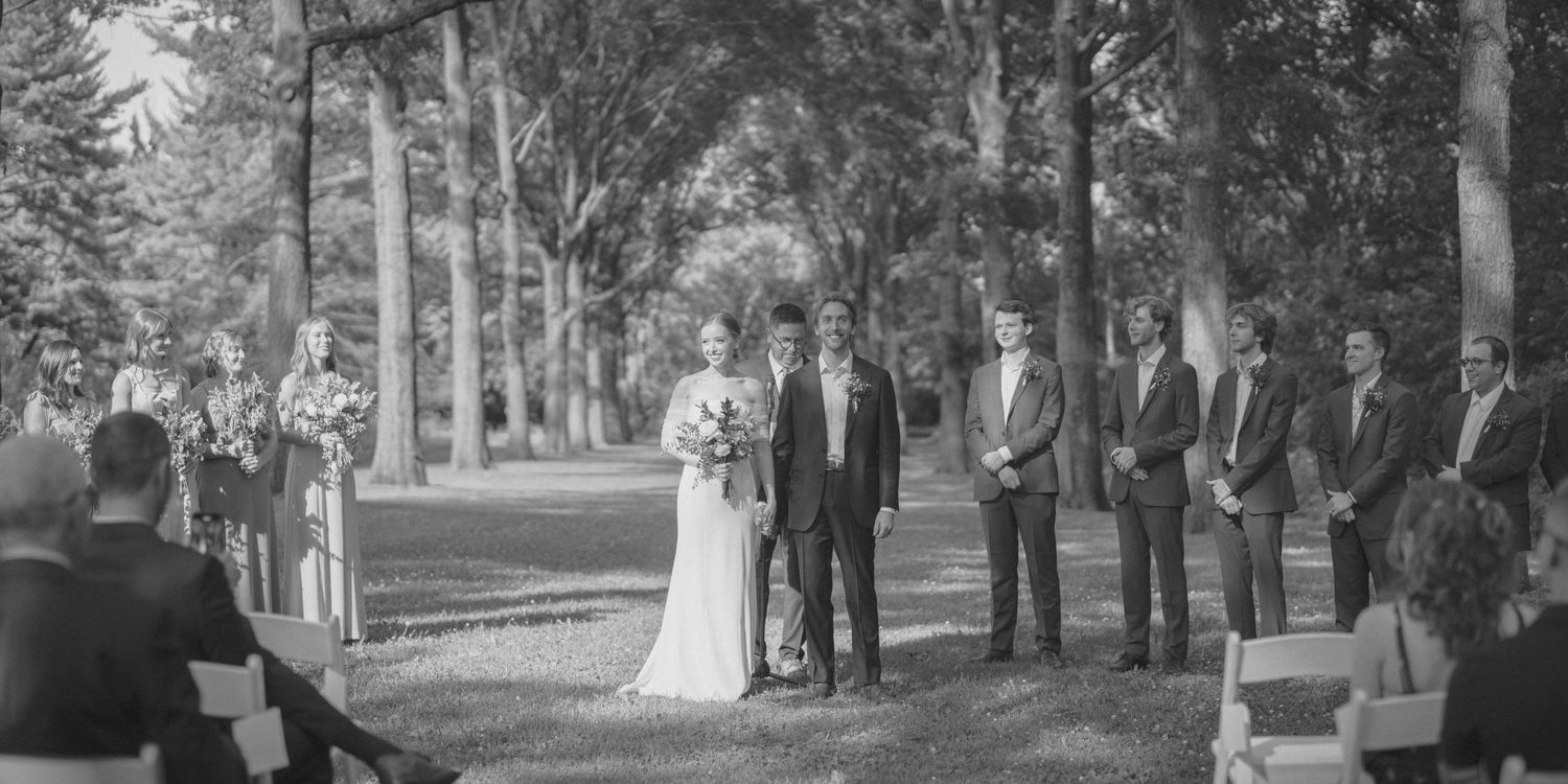 Bride and groom standing at outdoor wedding ceremony altar with groomsmen in black and white.