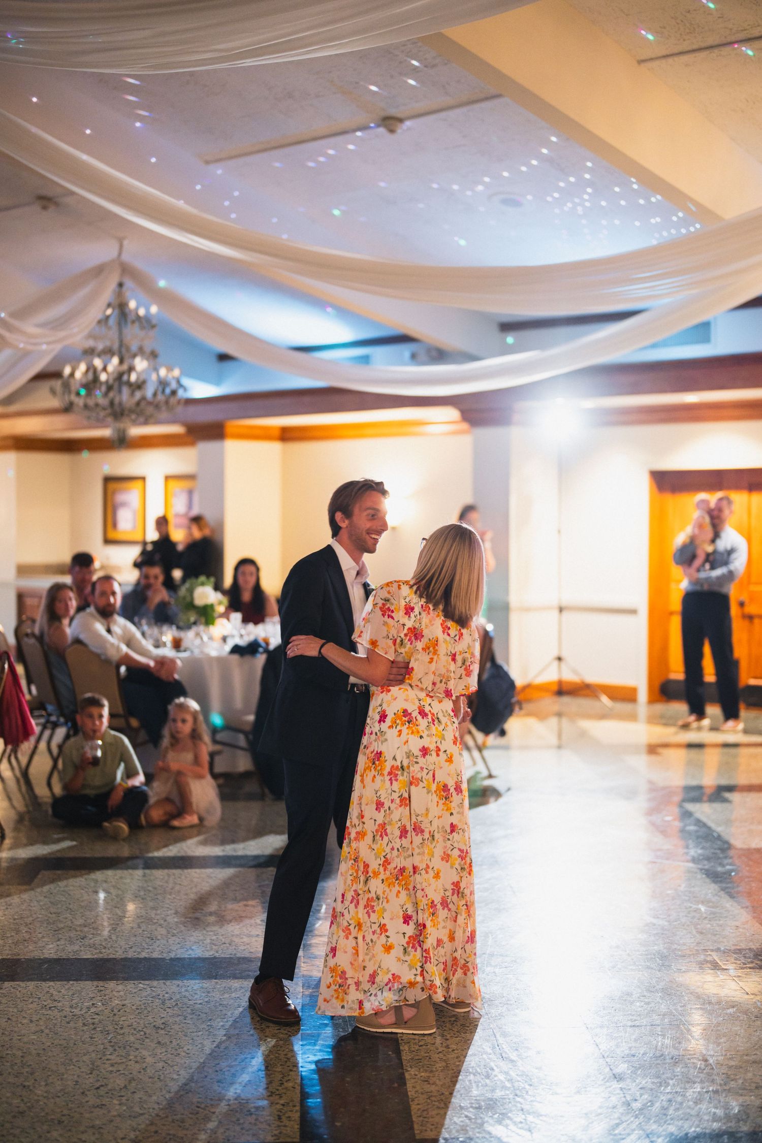 Groom dancing with his mother in a floral dress on the wedding reception dance floor.