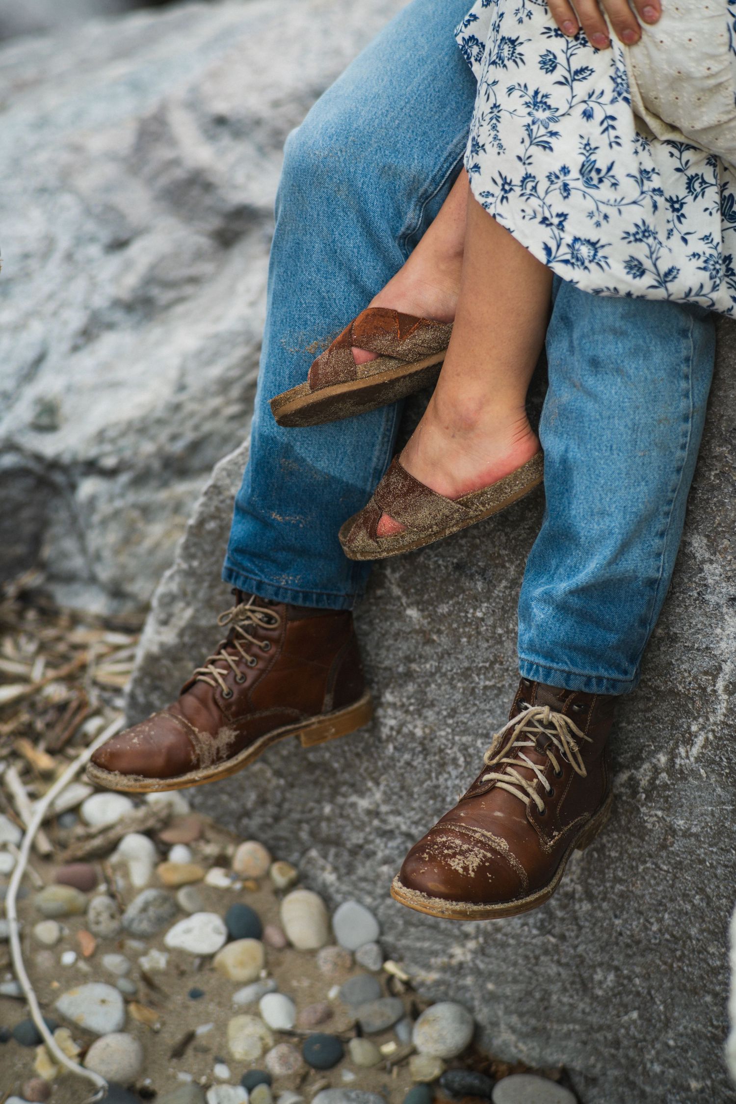 Close-up of couple's feet resting on rocks, wearing brown leather boots and sandals.