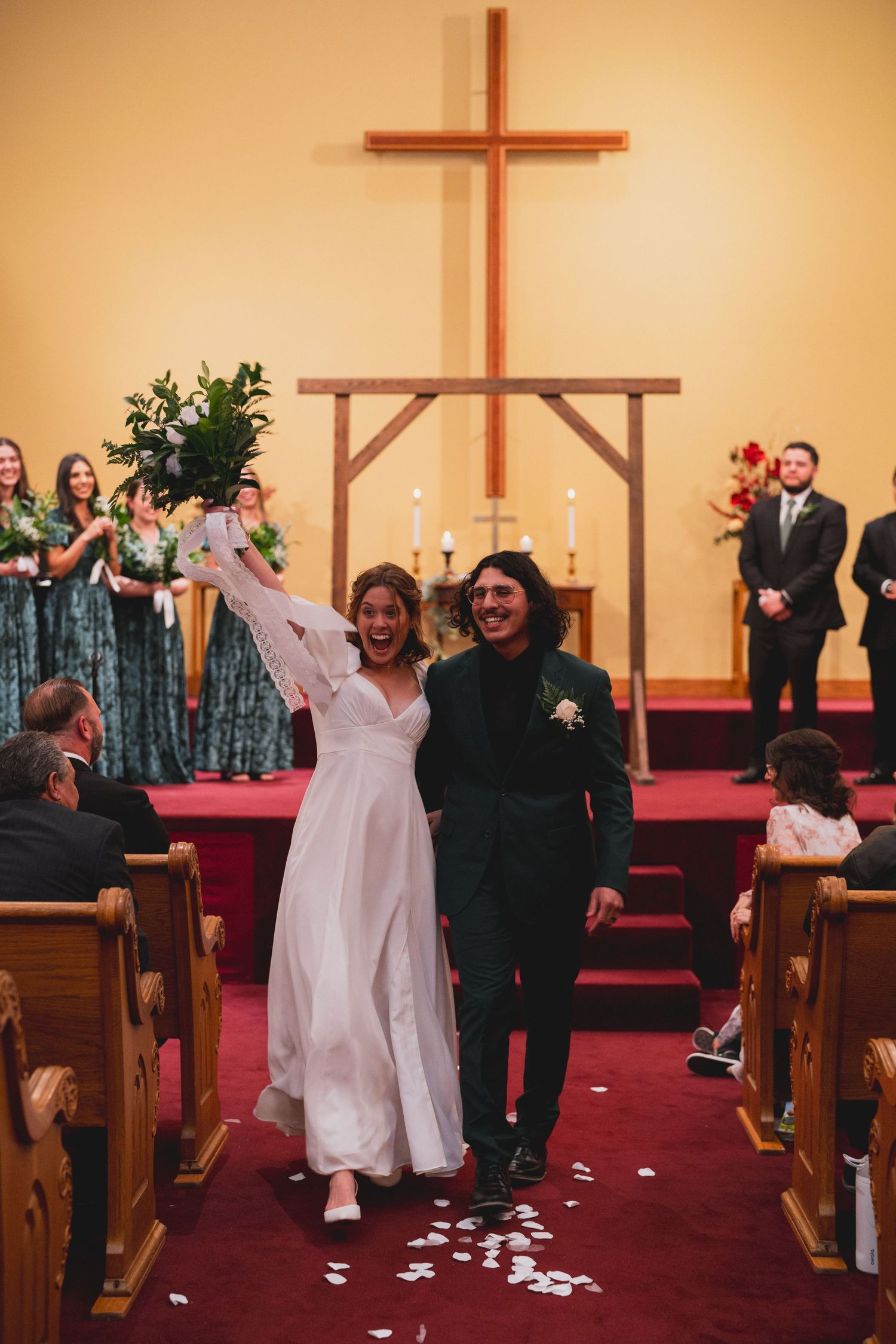 Happy couple exits down church aisle while guests in pews celebrate their union.