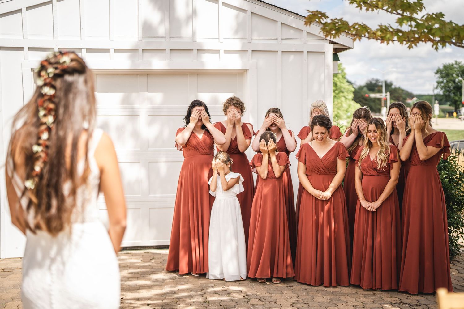 Wedding group photo with coordinated terracotta-colored dresses against white building.