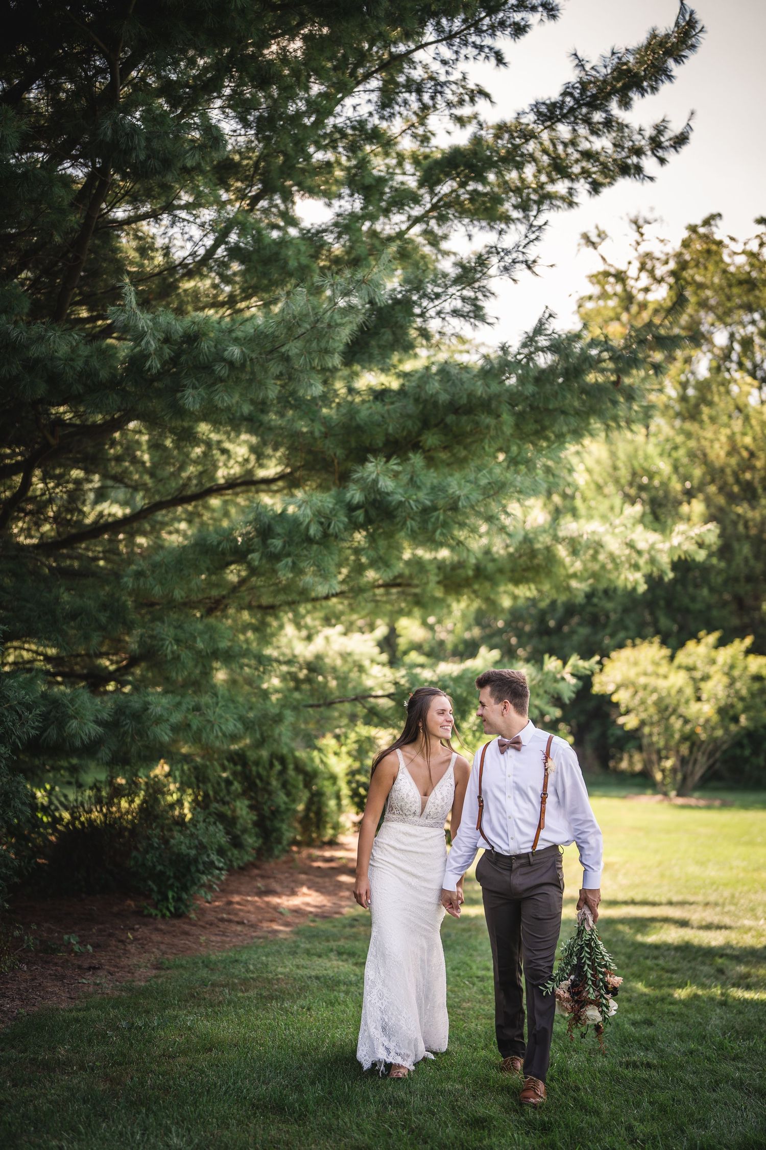 Couple walks hand in hand through a lush garden setting at sunset.