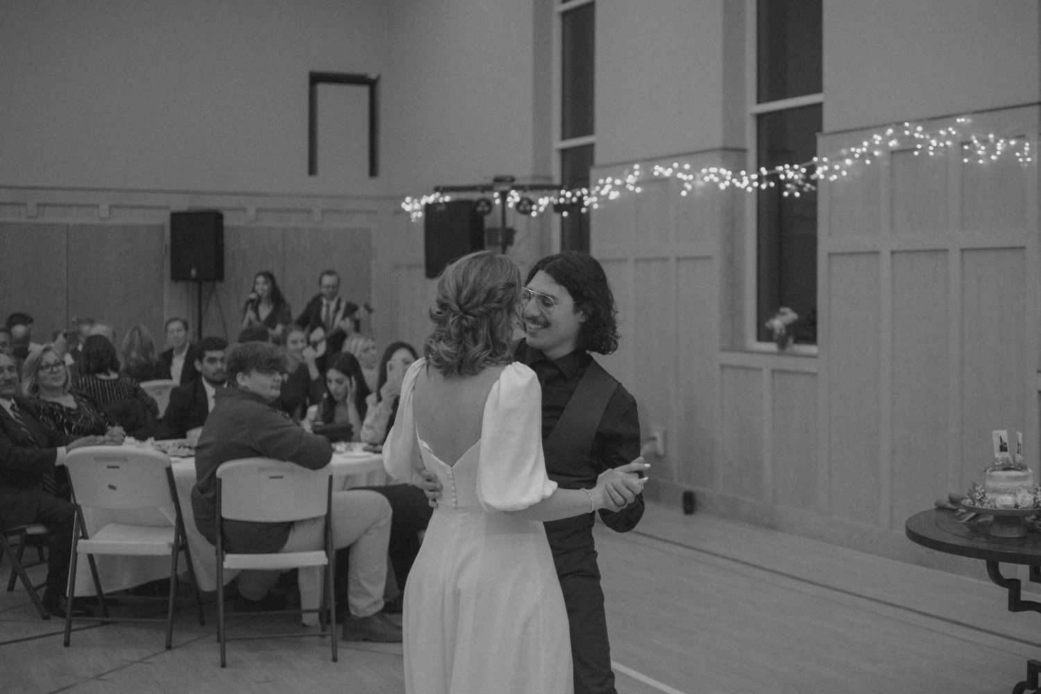 A couple shares their first dance in a reception hall decorated with twinkling lights.