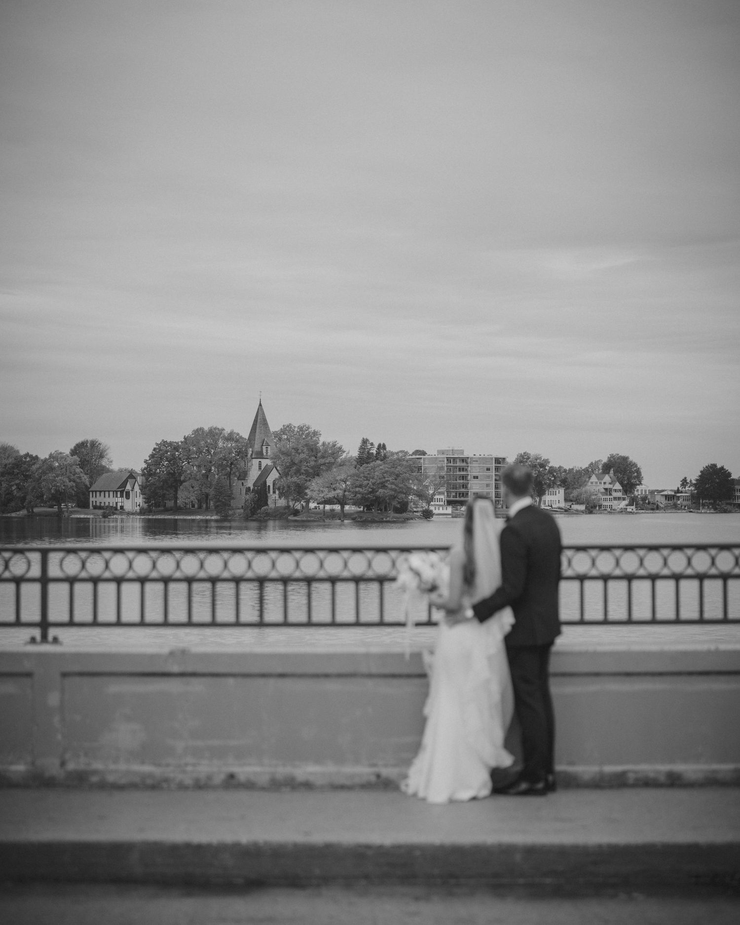Wedding couple silhouetted against waterfront with church spire in background.