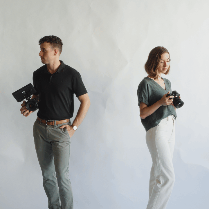 Studio video of photography and filmmaking duo glancing at each other then smiling at the camera.