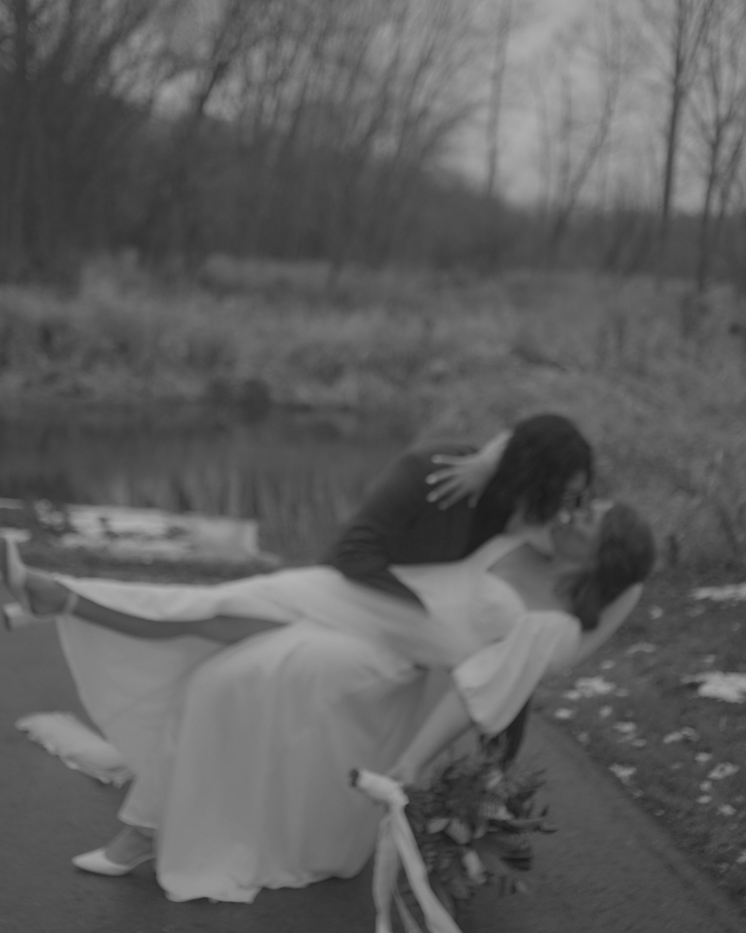 A romantic black and white photo of a couple sharing an intimate dip kiss near a pond.