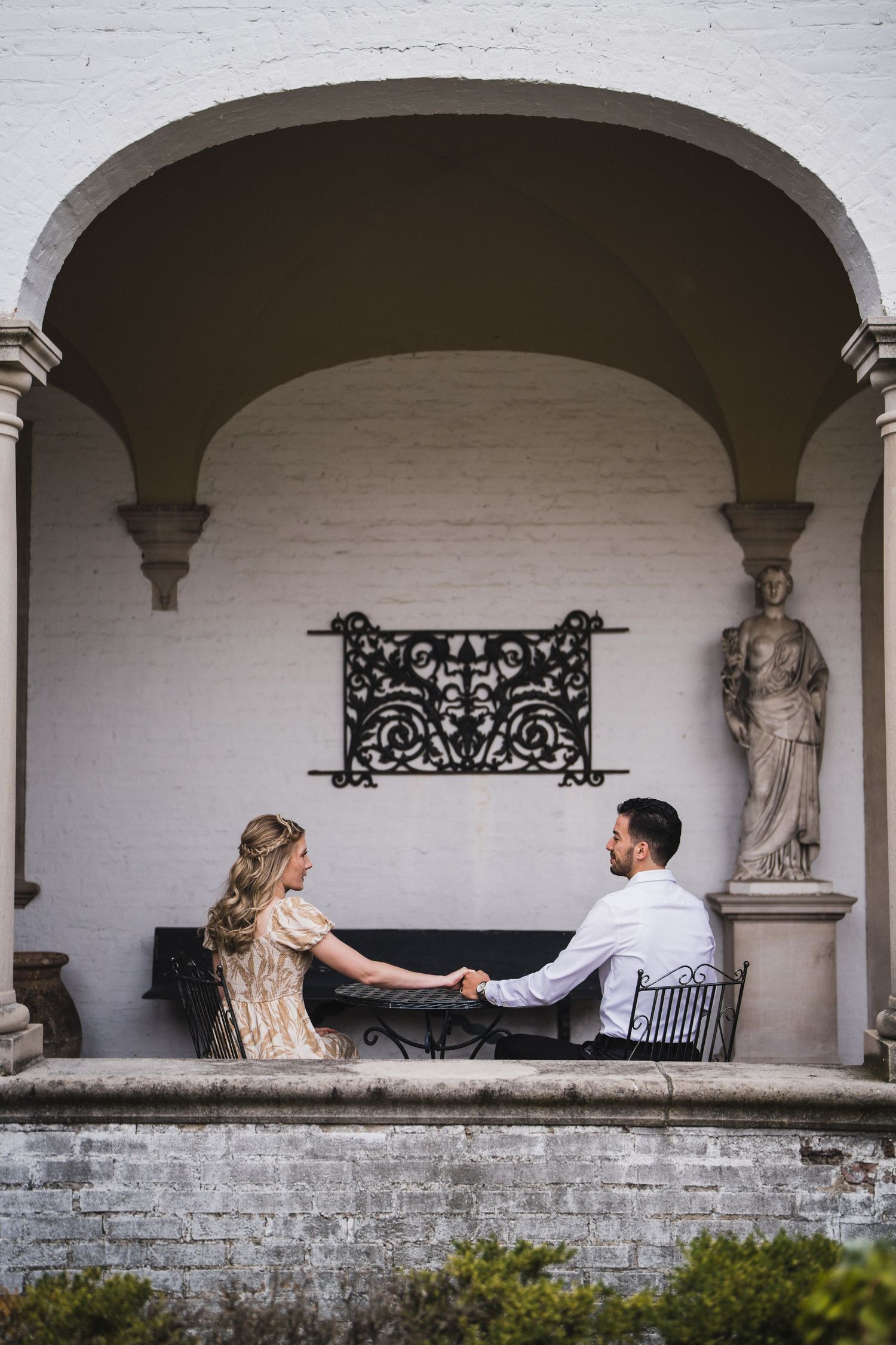 White arched colonnade with decorative ironwork and stone statues in a historic building.
