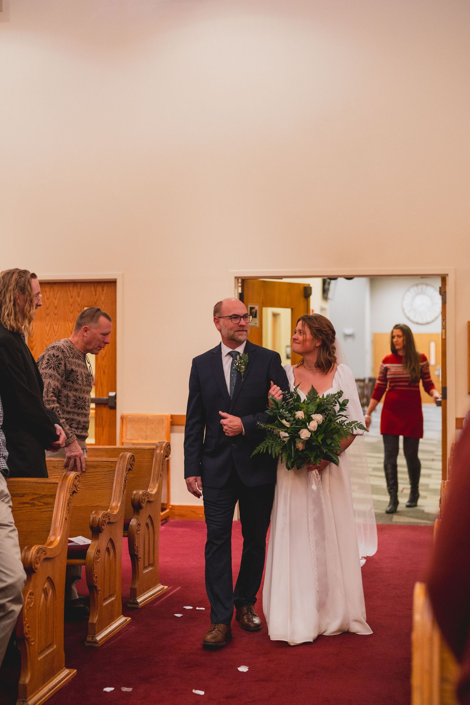 Wedding ceremony in progress inside church with red carpet and wooden pews.