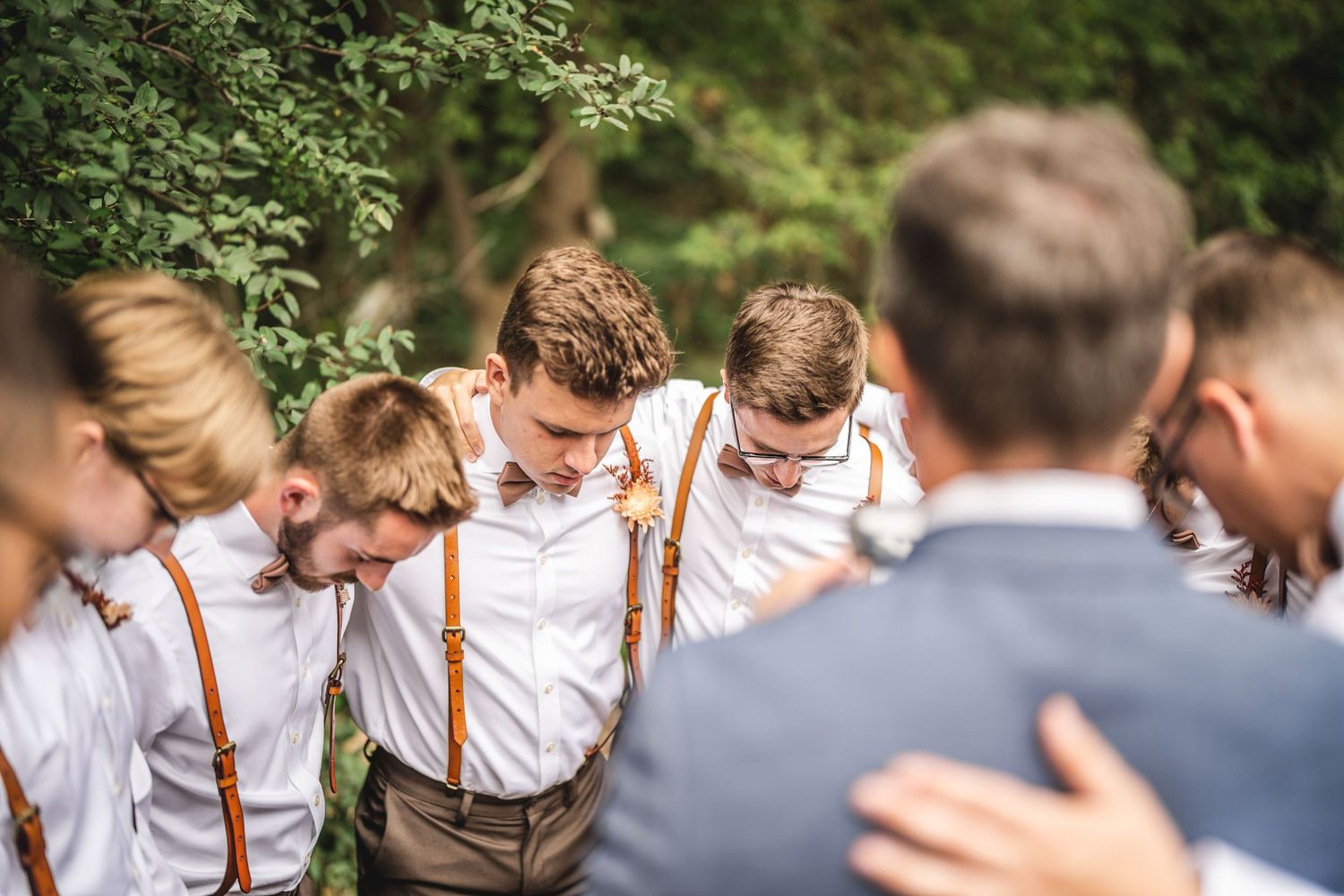 Wedding party members in suspenders and formal attire gathered outdoors.