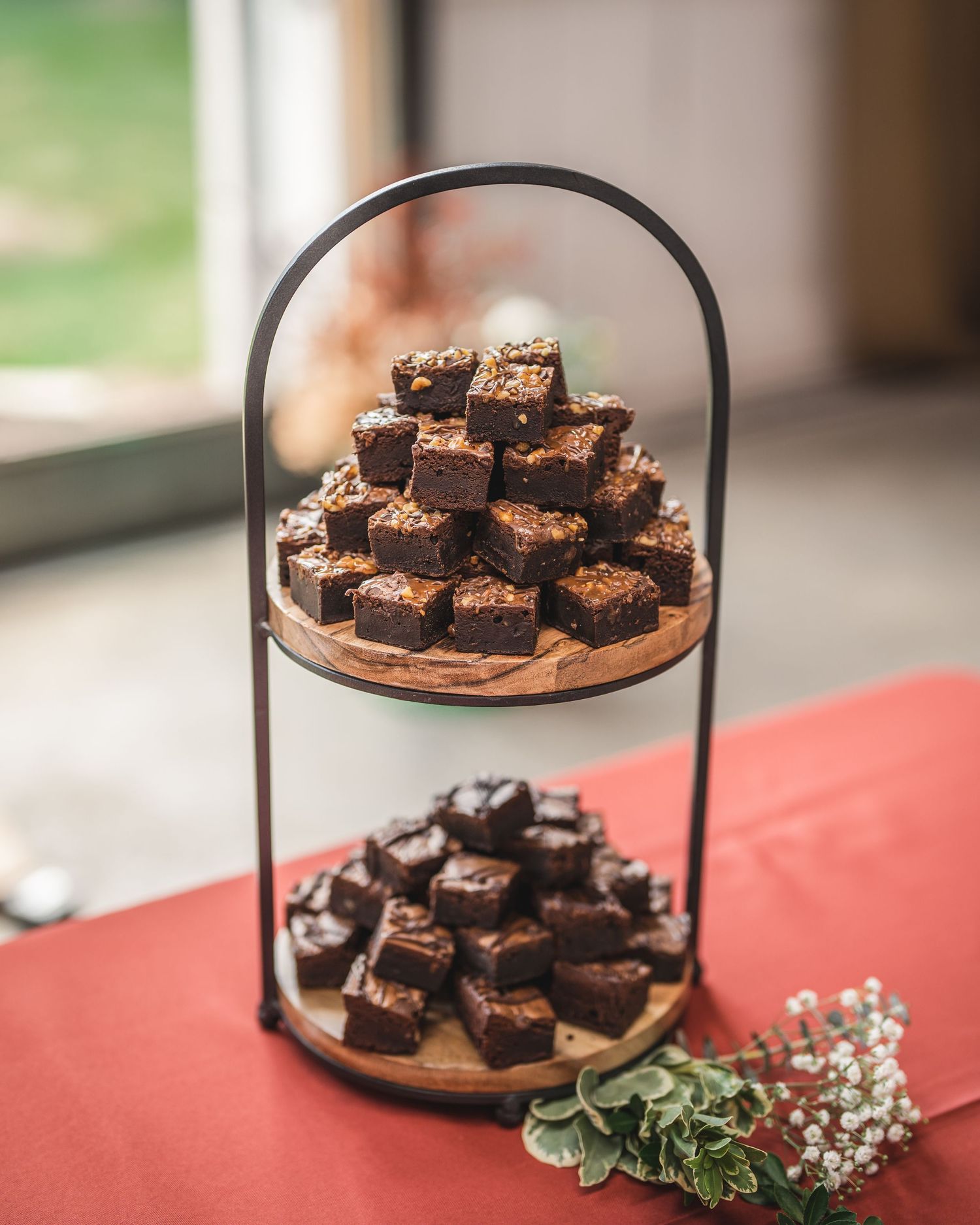 Tiered display of chocolate brownies on rustic wooden stand with greenery accents.