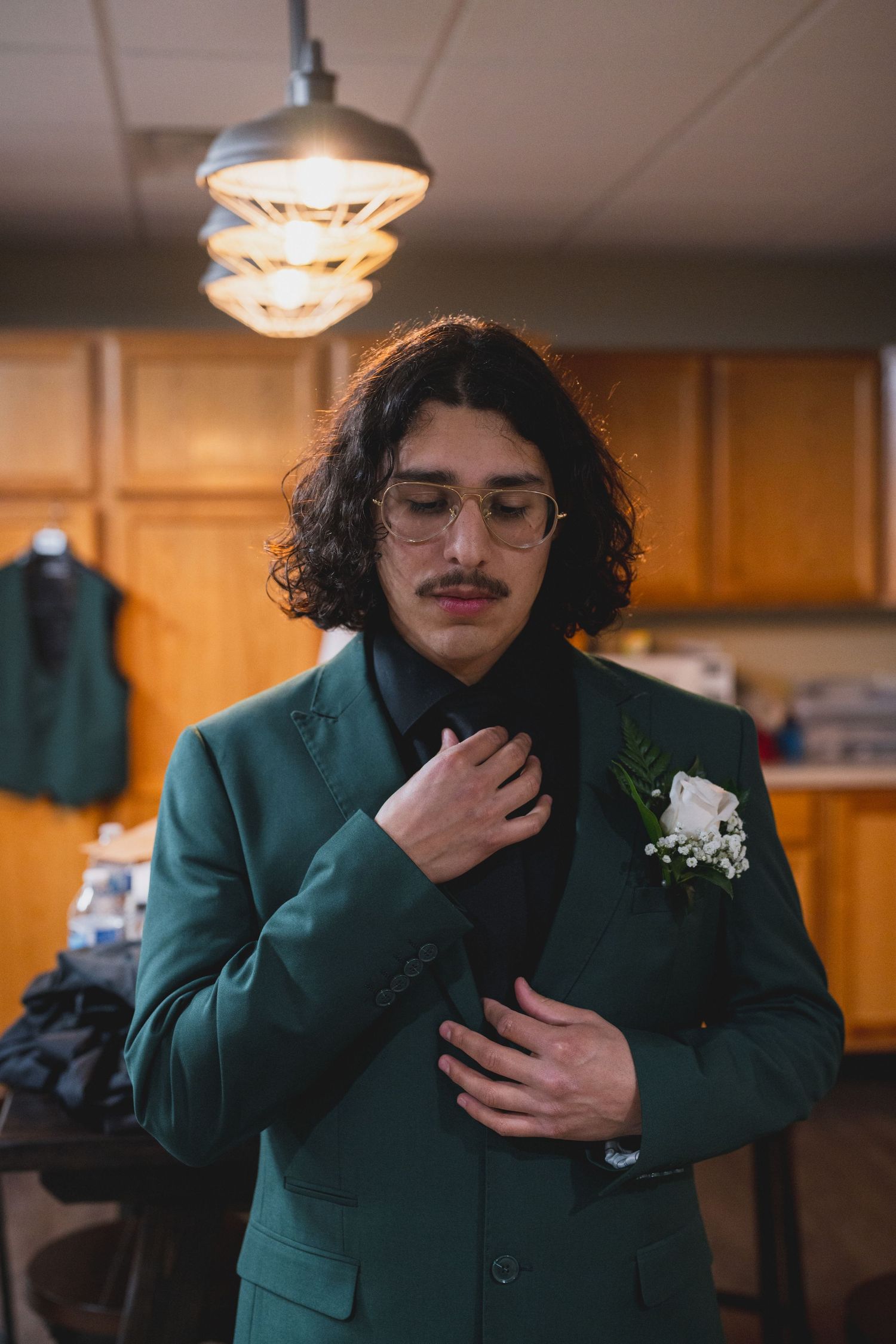 Person in emerald green suit jacket adjusts their tie while getting ready.