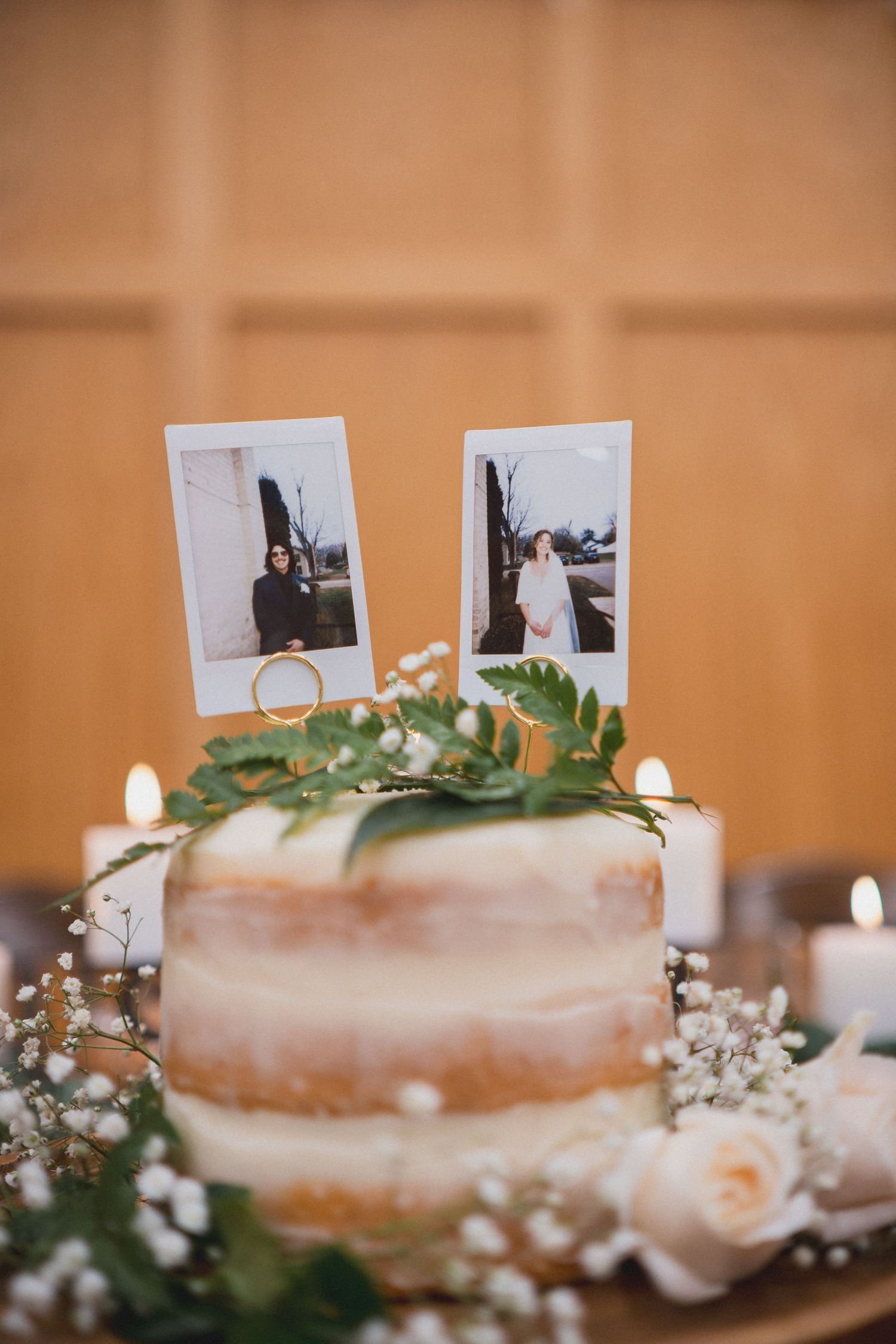 Wedding cake decorated with greenery and small photo decorations on top.