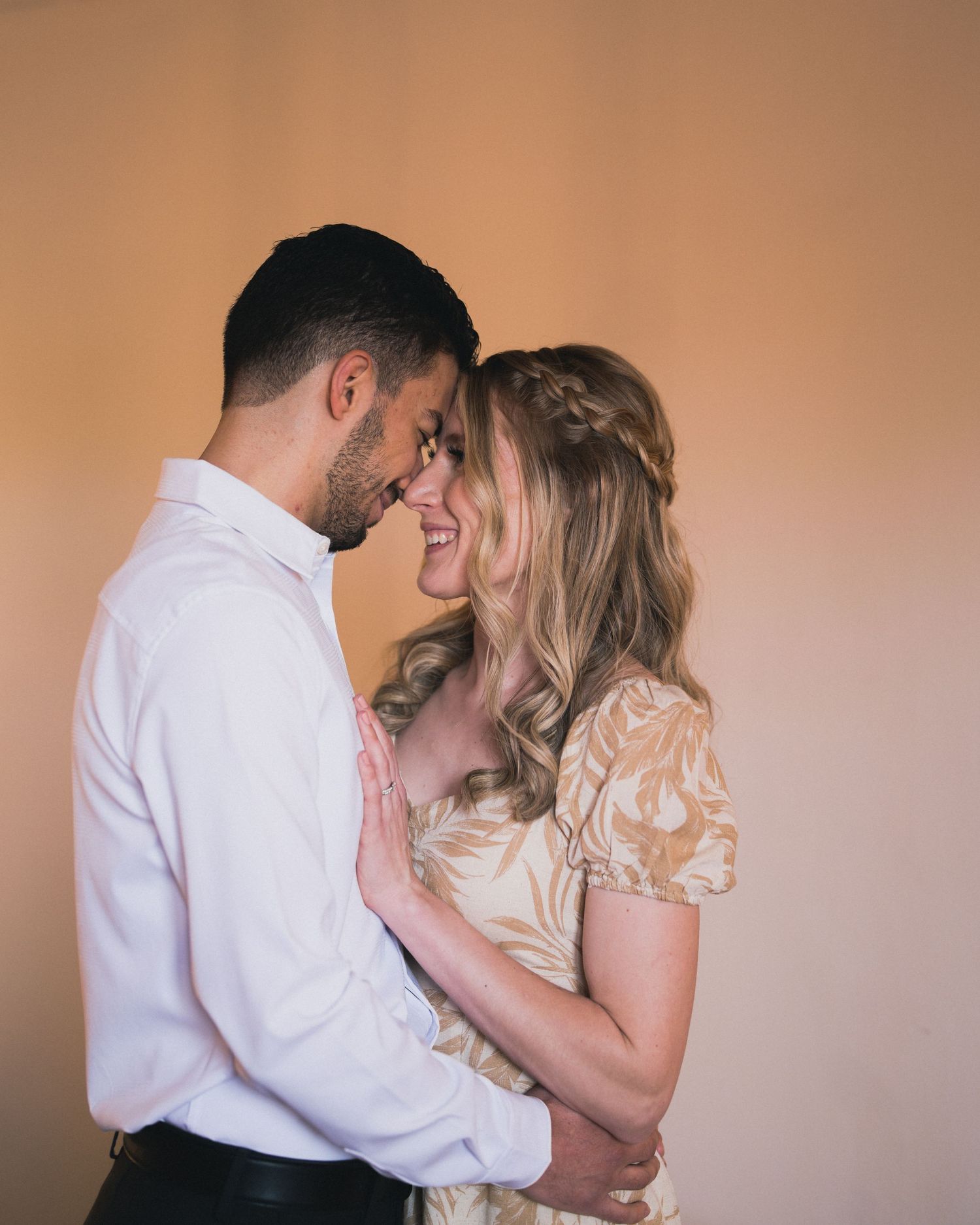 Intimate moment captured against warm peachy background in romantic setting.