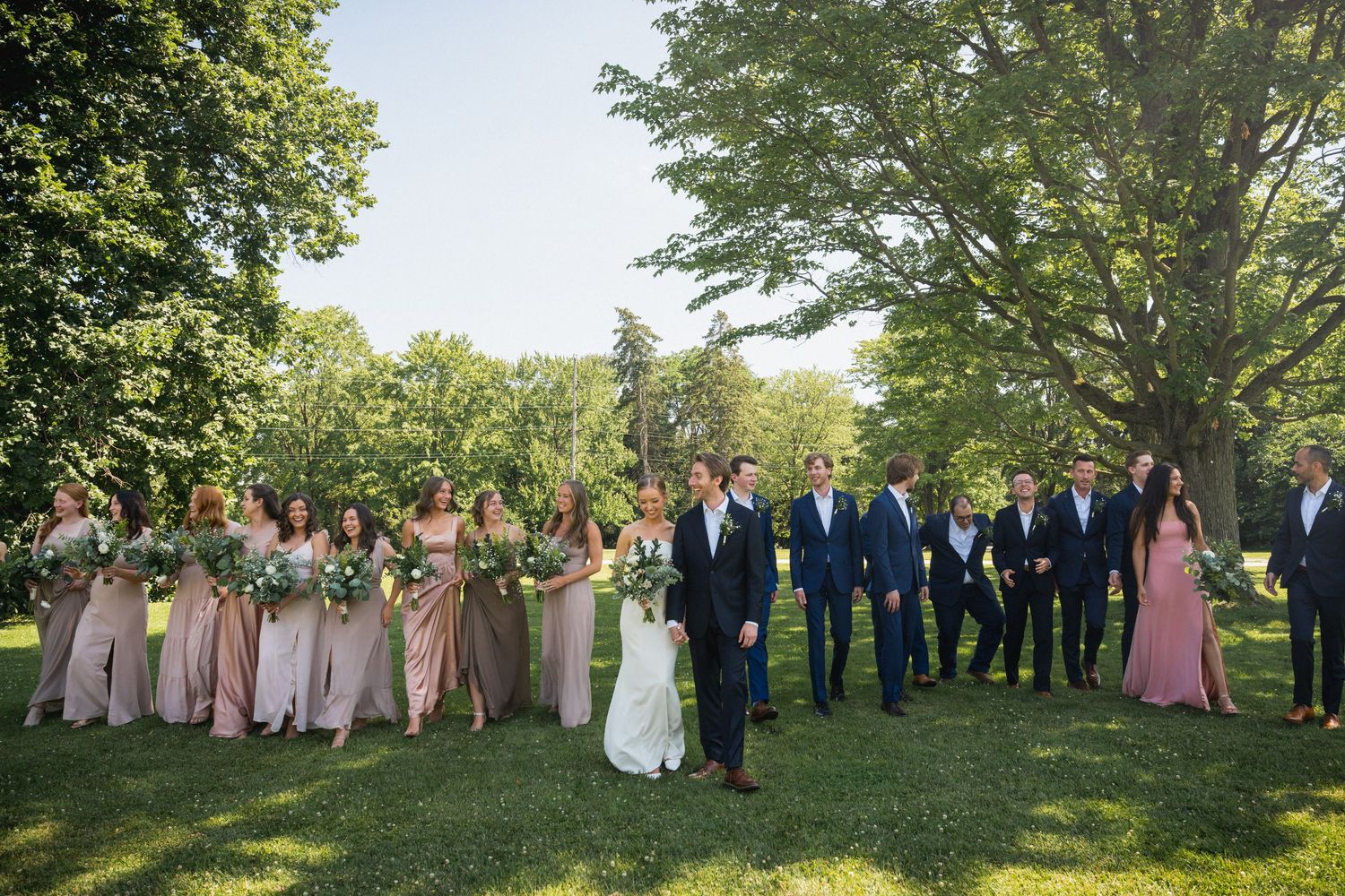 Wedding party walking together outdoors, bridesmaids in pink dresses and groomsmen in blue suits.