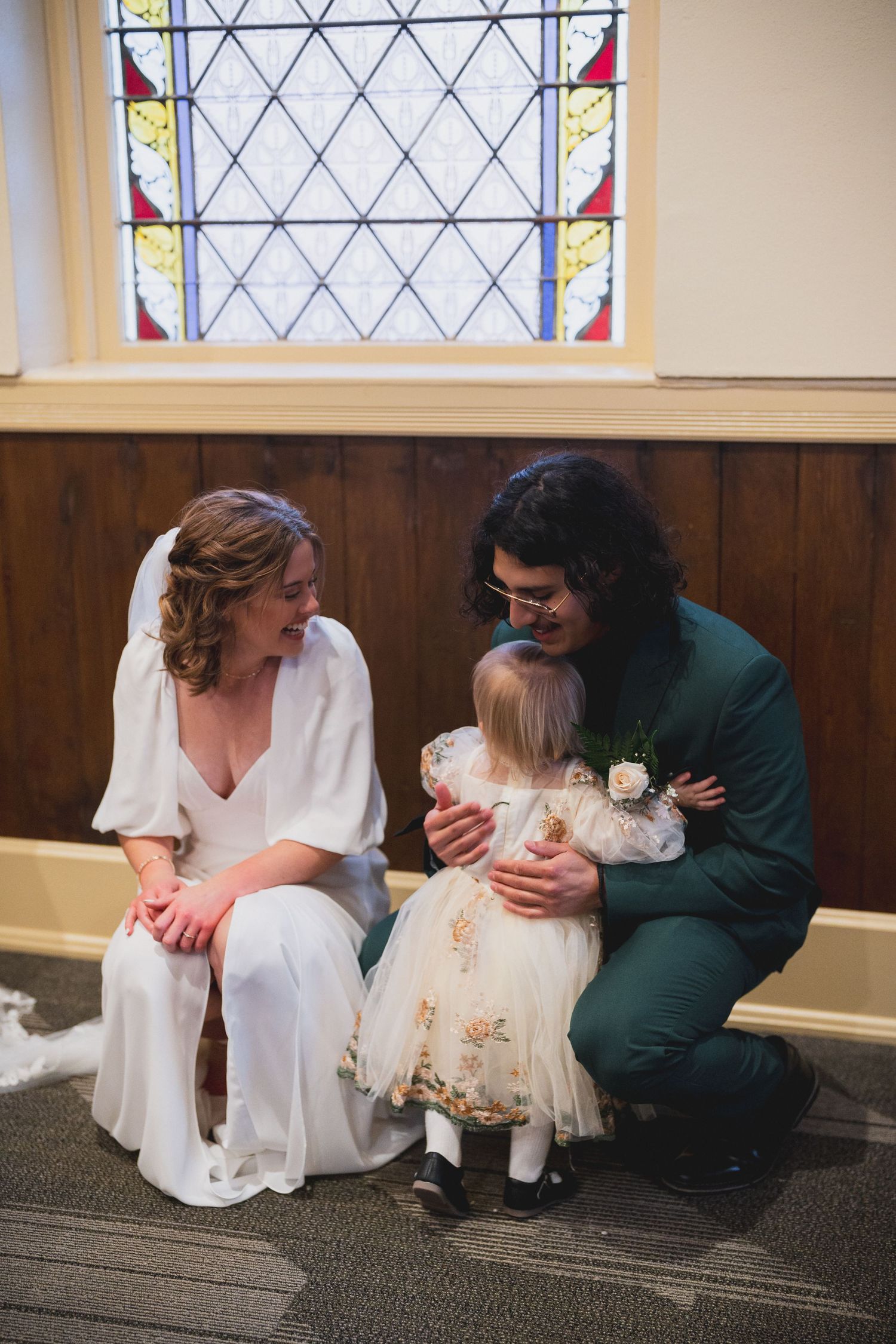 Wedding couple sitting beneath stained glass window sharing an intimate moment.