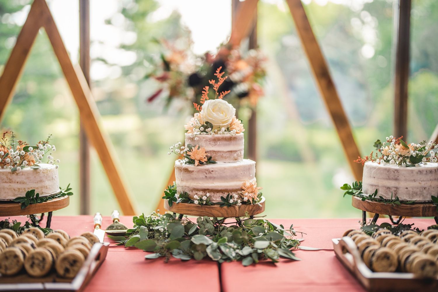 Wedding dessert table featuring pink tiered cakes and floral decorations against natural backdrop.