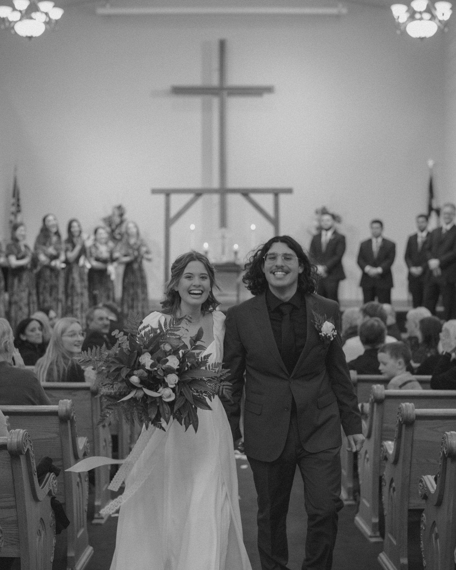 Black and white photo of jubilant newlyweds walking down church aisle after ceremony.