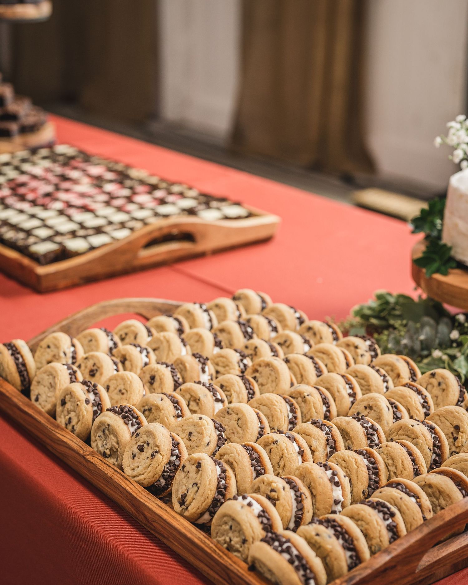 Wooden board filled with rows of homemade chocolate chip cookies on red tablecloth.