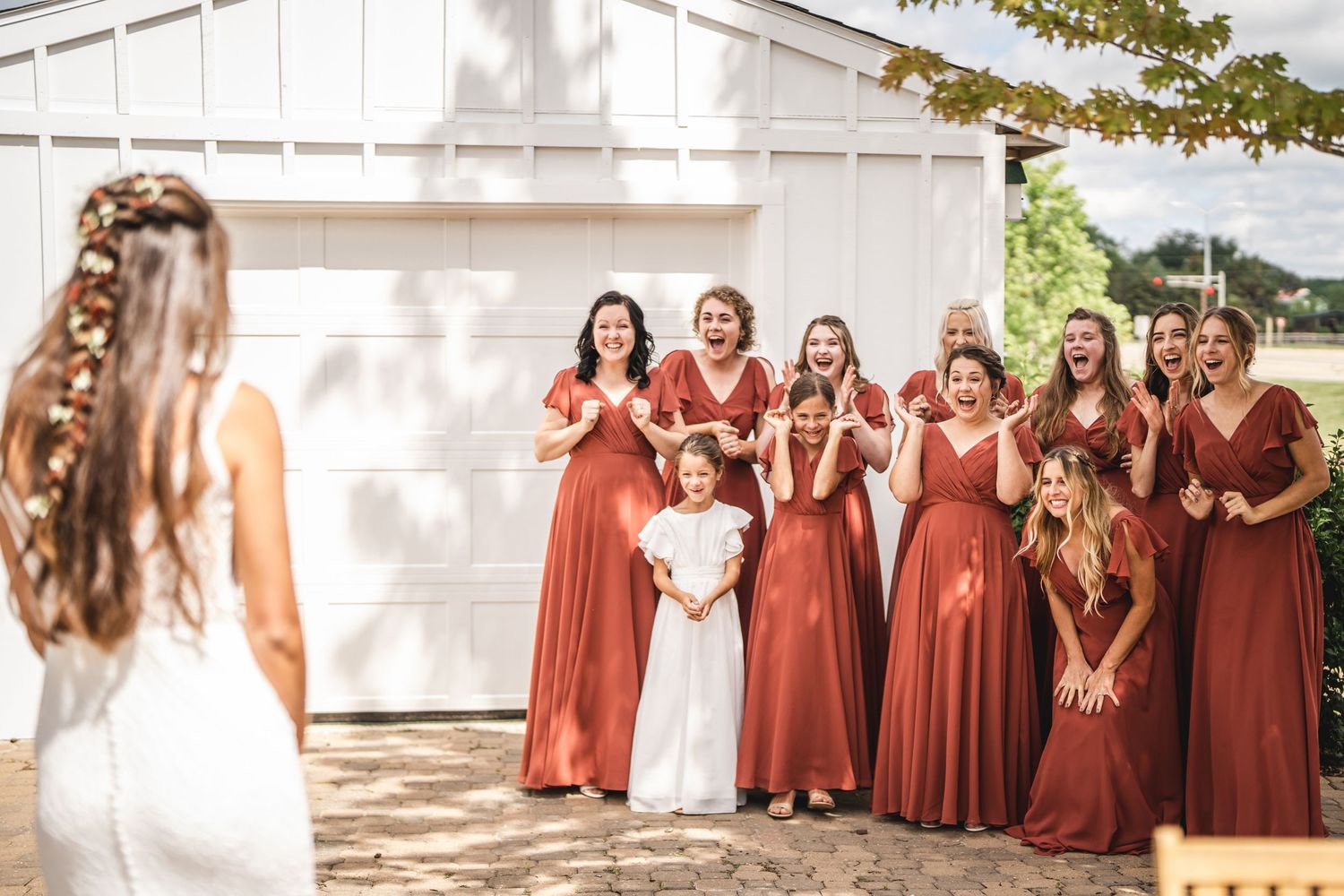 Wedding party in matching rust-colored dresses posing outdoors.