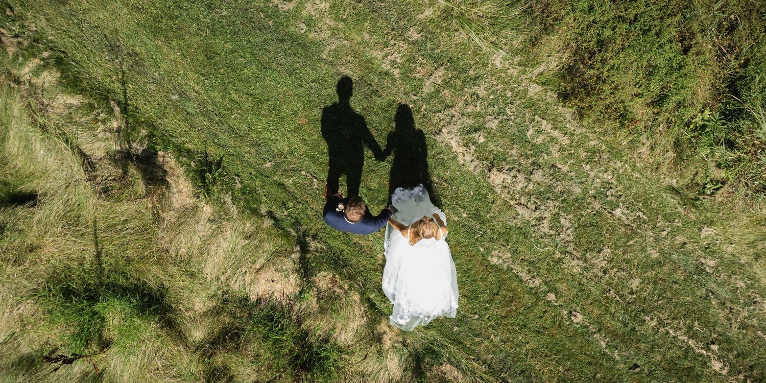 An aerial view of newlyweds walking together on a grassy hillside.