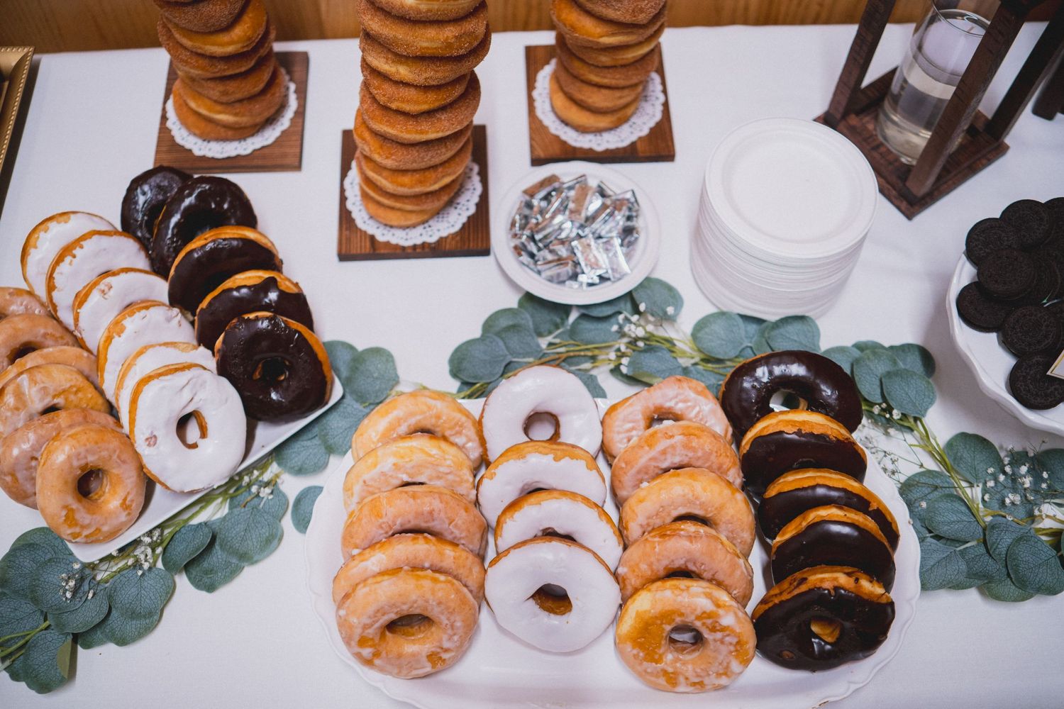 An assortment of donuts arranged on platters with eucalyptus leaves for decoration.