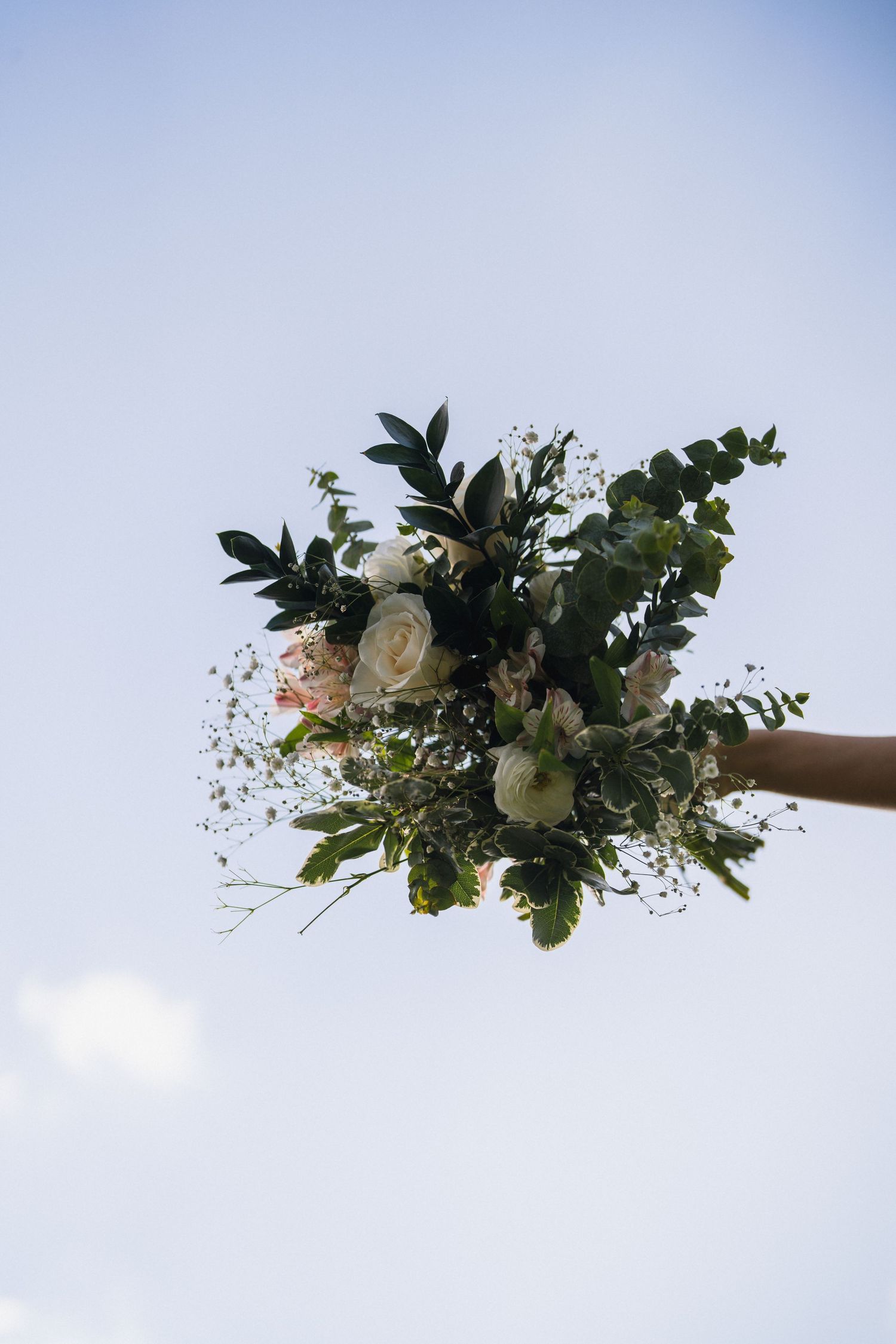 A beautiful wedding bouquet with white roses and eucalyptus held up against a blue sky.