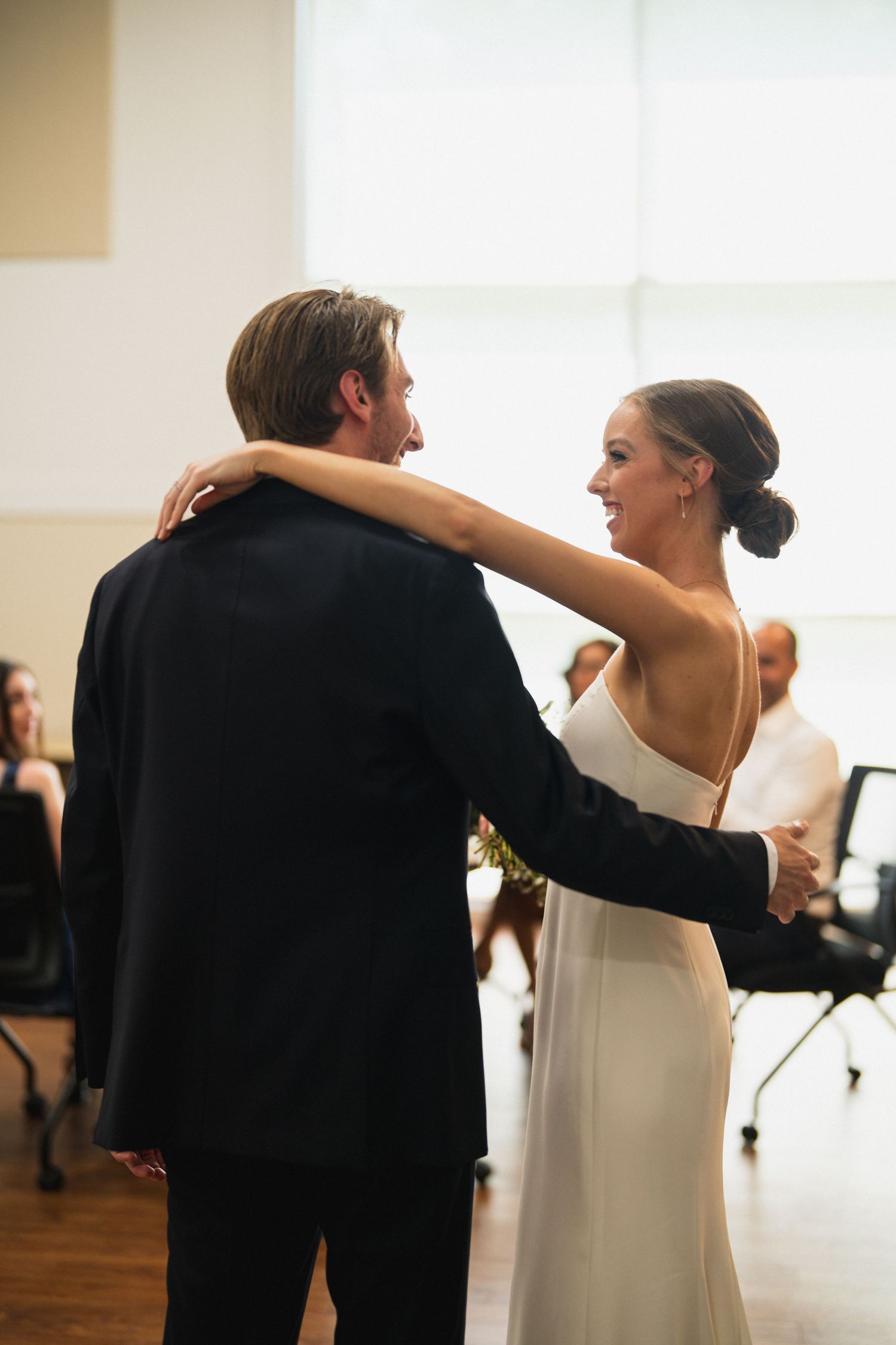 Bride and groom share their first dance, smiling joyfully in an elegant indoor wedding reception.