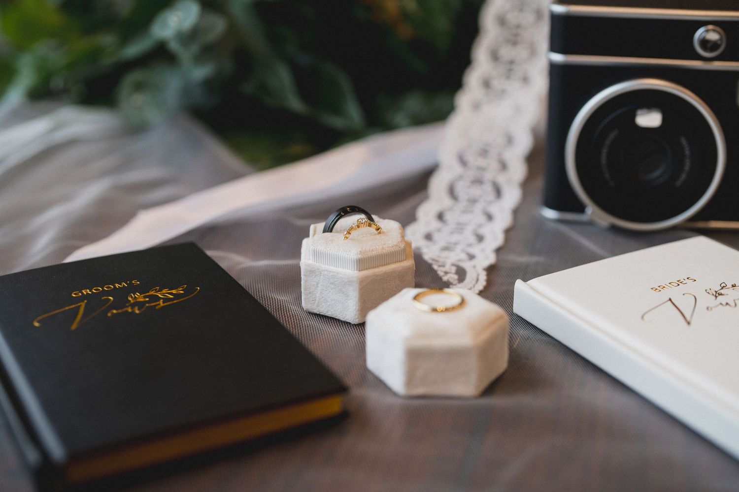 Wedding vow books and ring boxes arranged with vintage camera on wooden surface.
