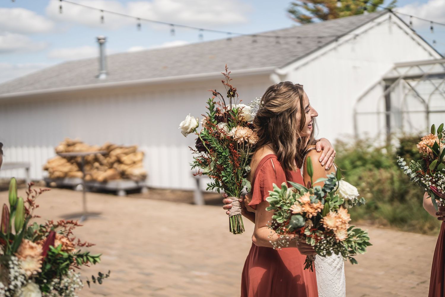 Wedding party members hold beautiful peach and green floral bouquets outdoors.