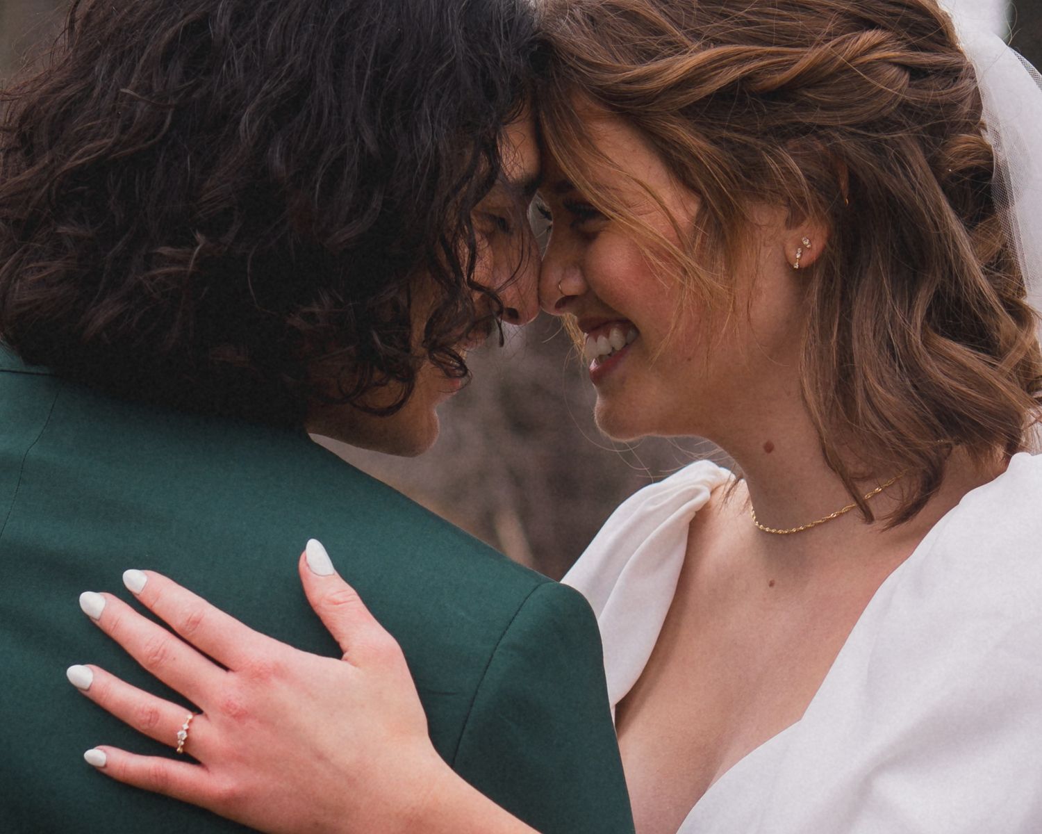 Two people share an intimate moment in wedding attire against a natural outdoor backdrop.