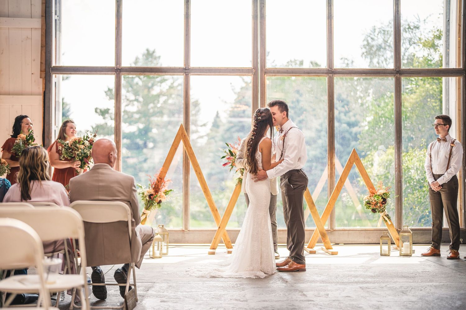 Wedding party poses playfully in a bright sunlit venue with large windows and wooden beams.