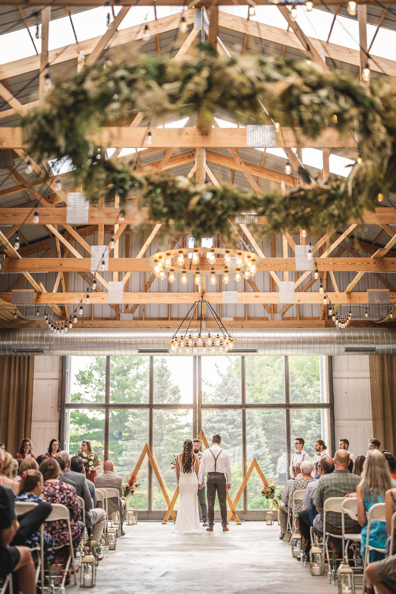 Wedding venue with rustic wooden beams, greenery garlands, and chandeliers overlooking ceremony setup.