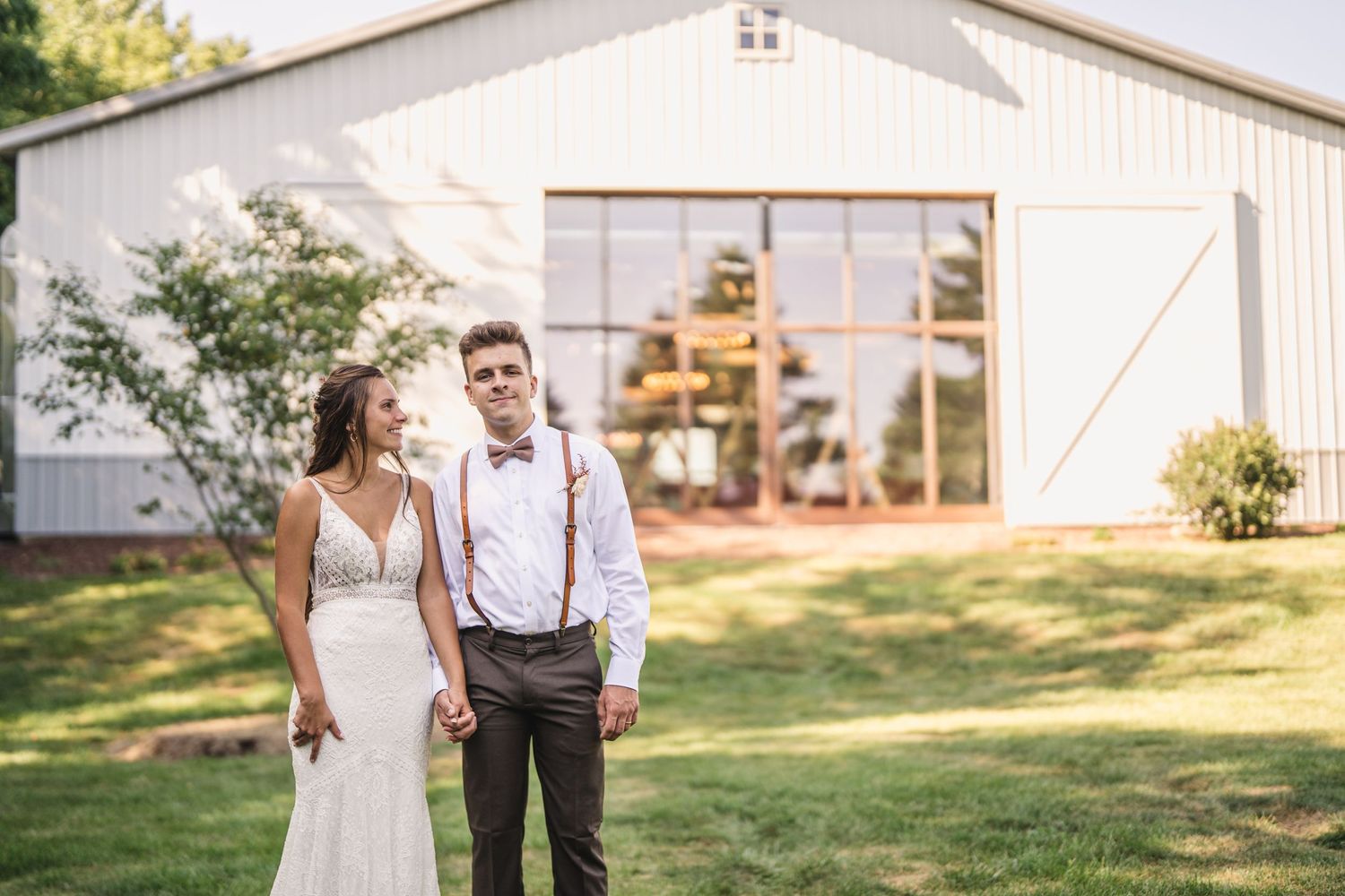 A couple in wedding attire standing in front of a rustic white barn.