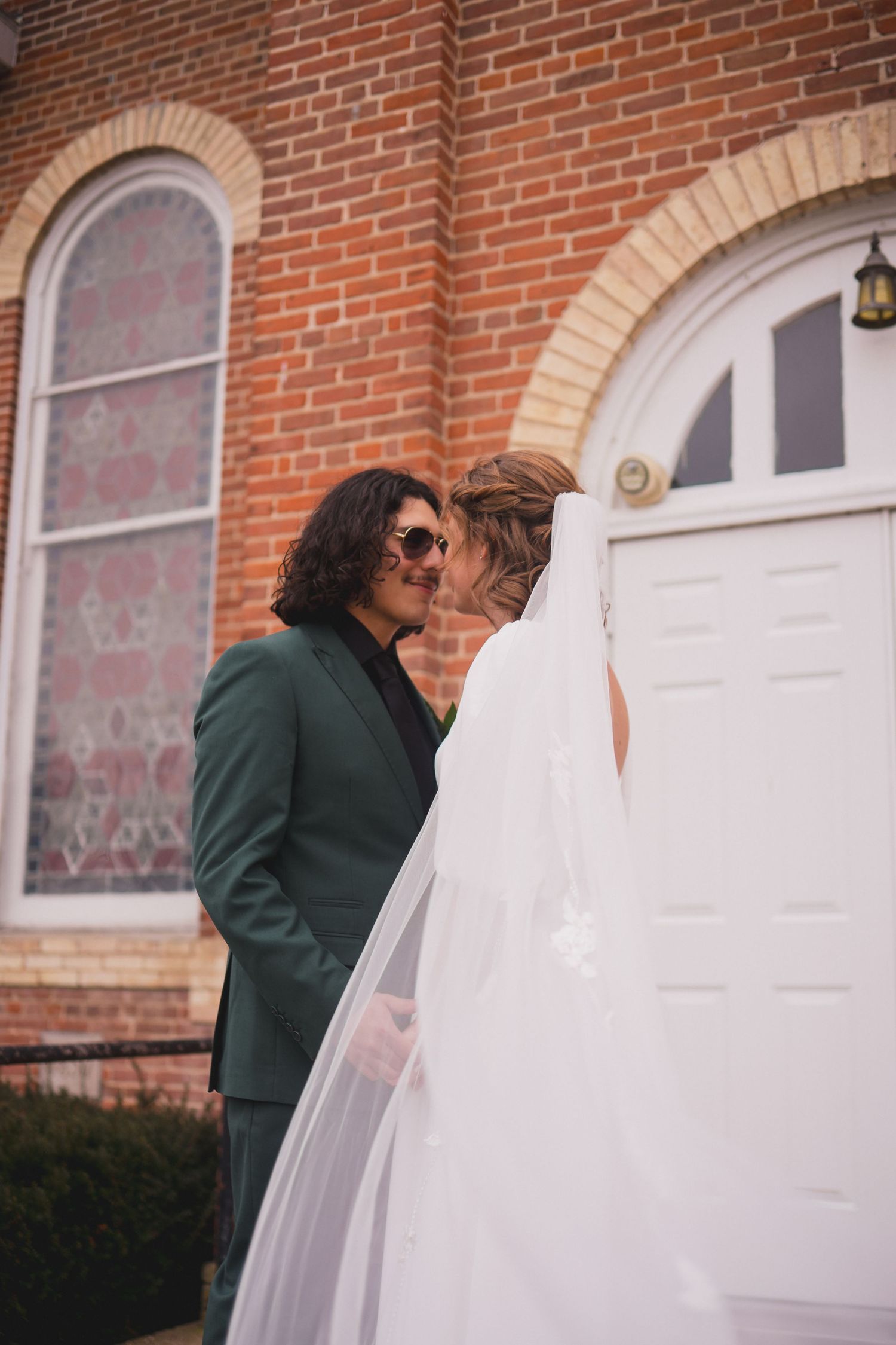 Wedding couple standing in front of a historic brick building with arched windows.