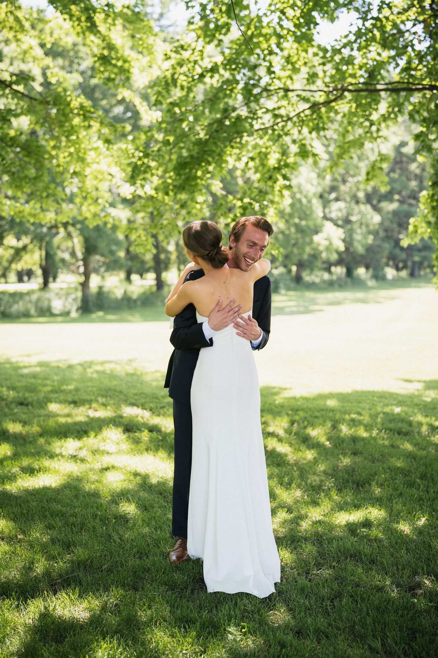 Bride and groom share a romantic embrace in a lush green park on their wedding day.