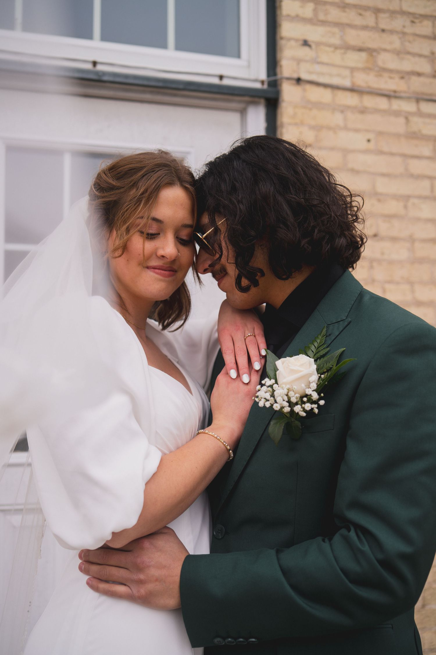 A romantic wedding moment with a couple embracing, featuring an emerald green suit and white bridal gown.
