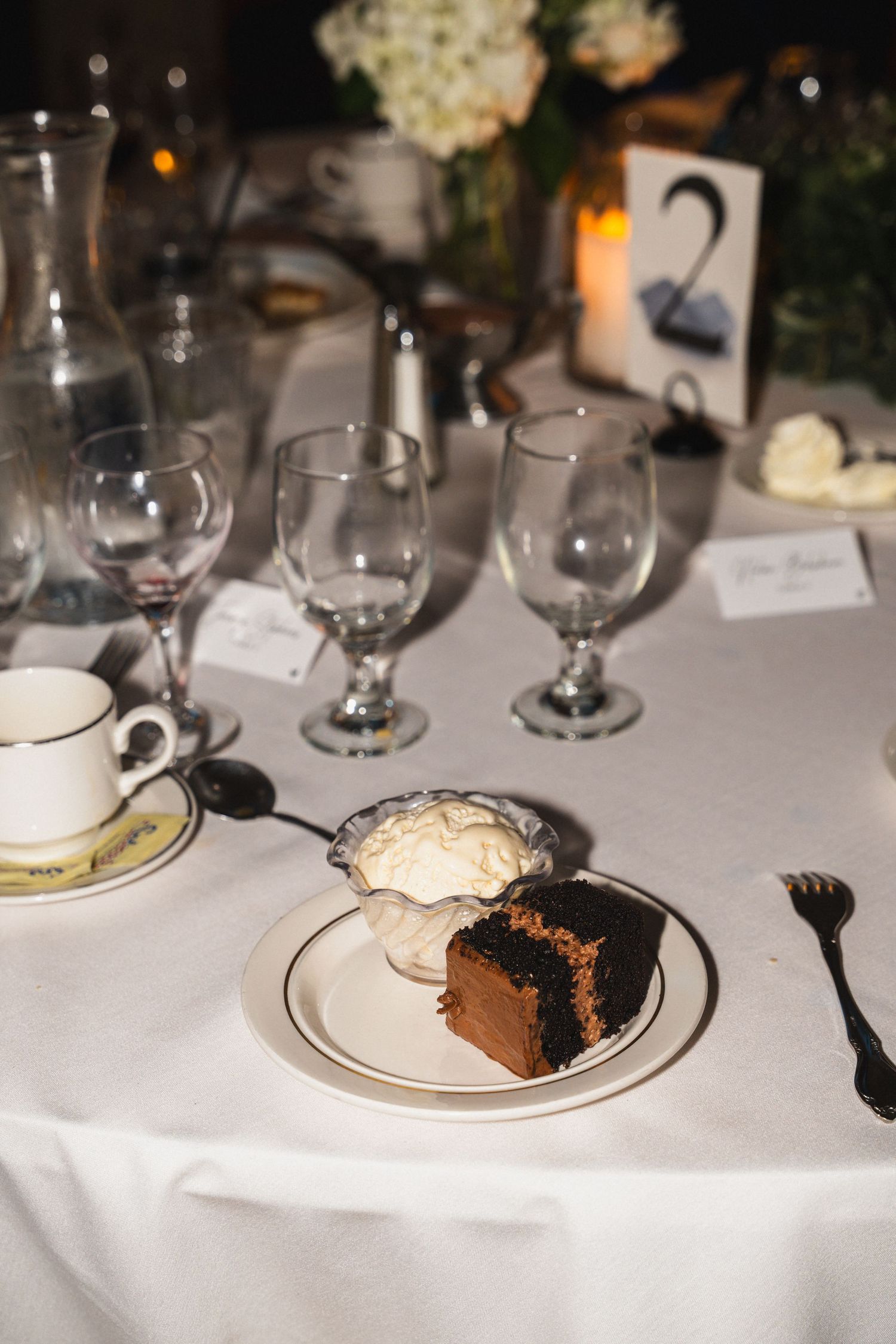 Elegant wedding reception table set with chocolate cake, white linens, and crystal glassware.