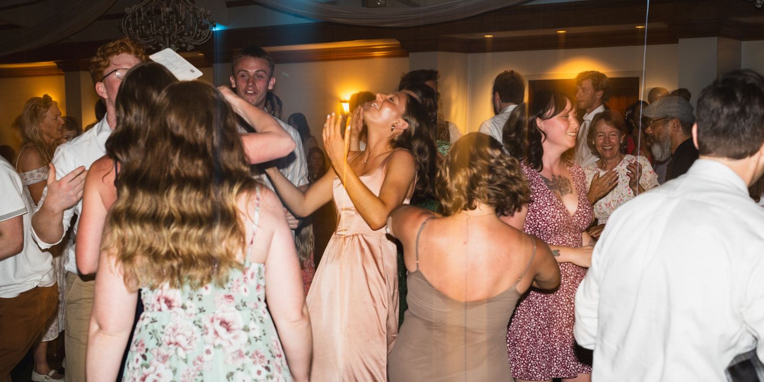 Energetic wedding reception dance floor with guests dancing and celebrating in elegant venue.
