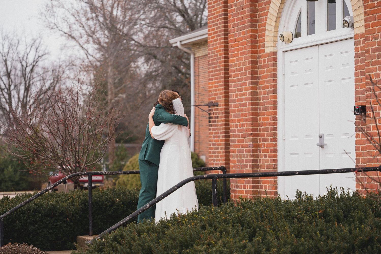 Winter wedding scene with a couple posing outside a traditional brick church.