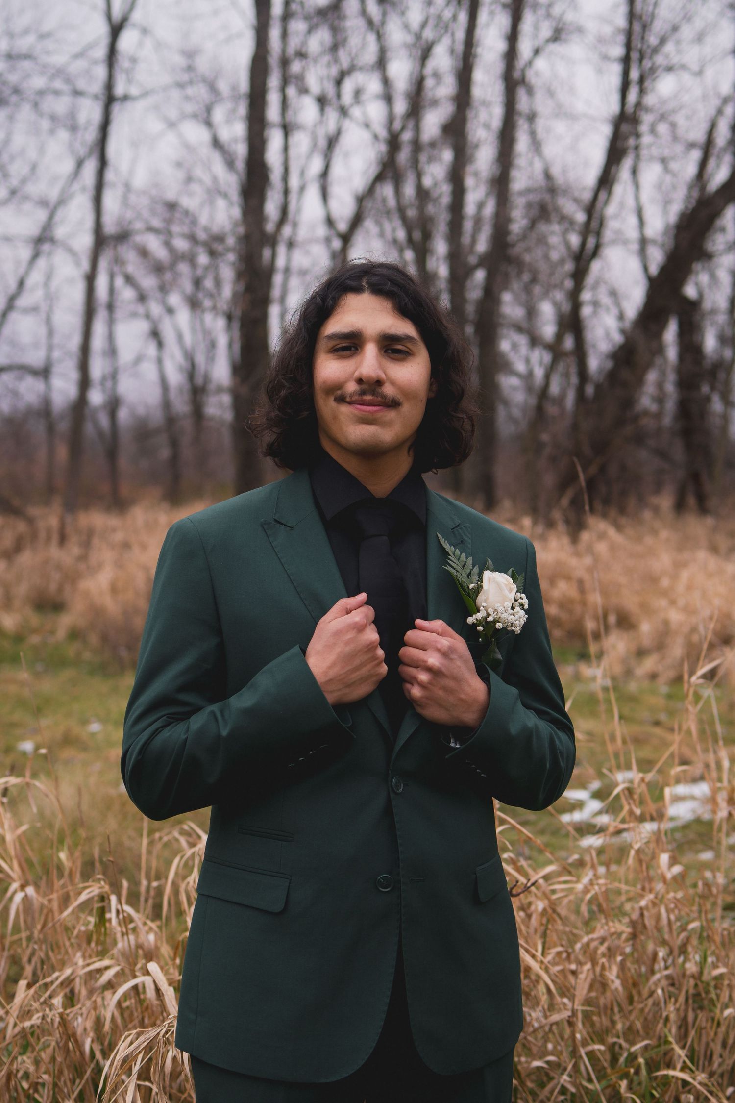 Portrait of person in emerald green suit adjusting jacket lapels against autumn landscape.