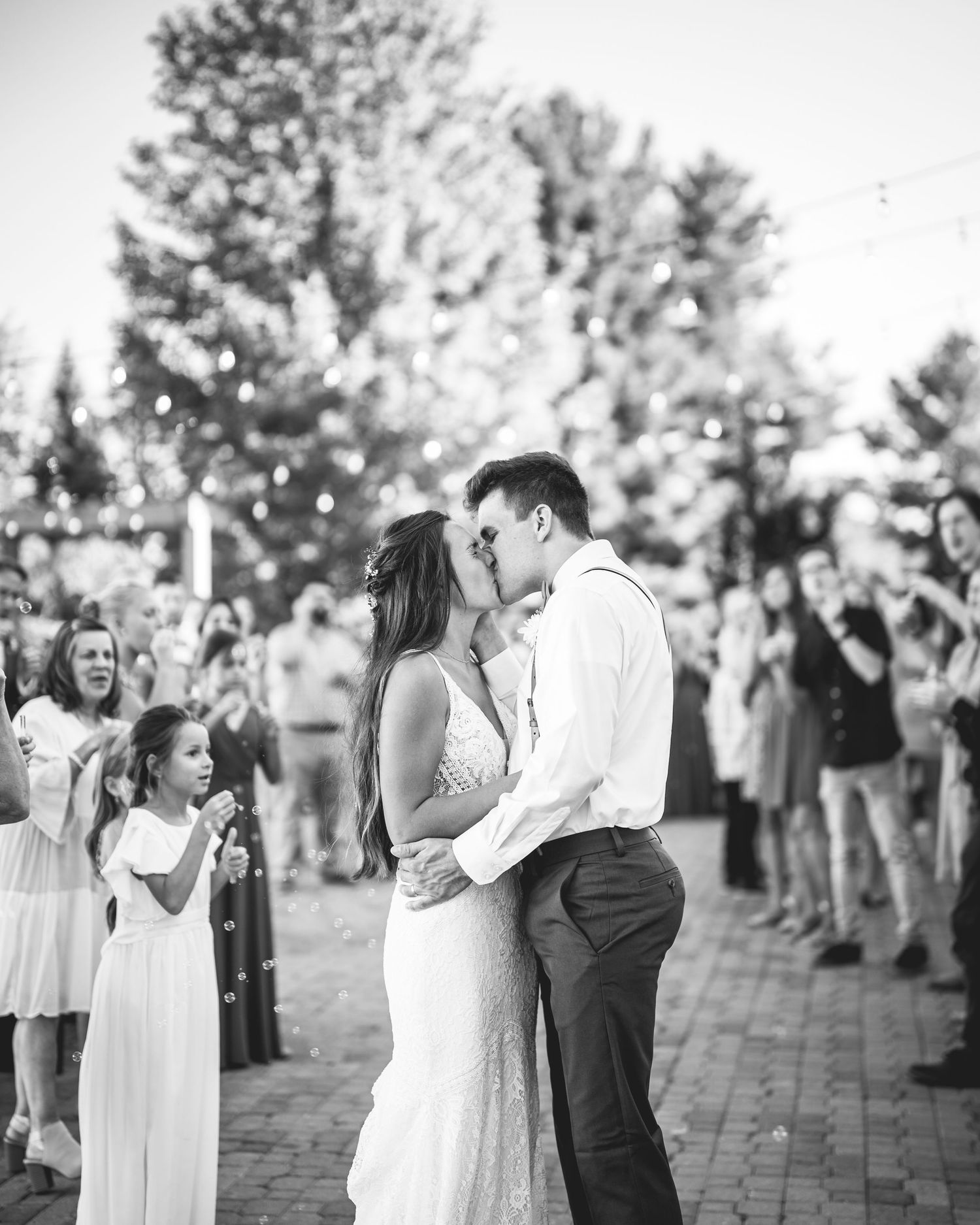 Black and white photo of wedding couple dancing surrounded by guests at outdoor reception.