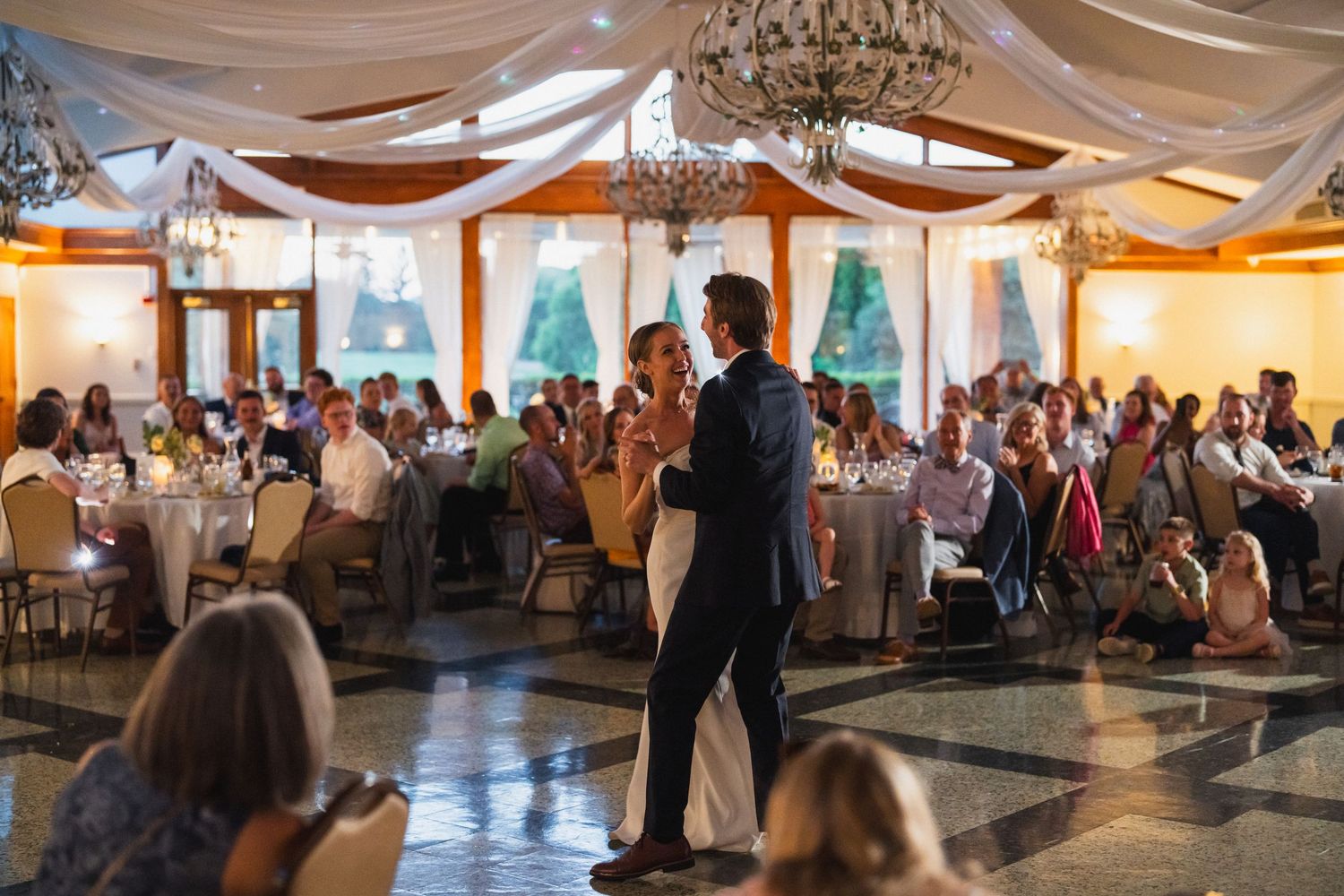 Newlyweds share a romantic first dance while wedding guests watch in a beautifully decorated venue.